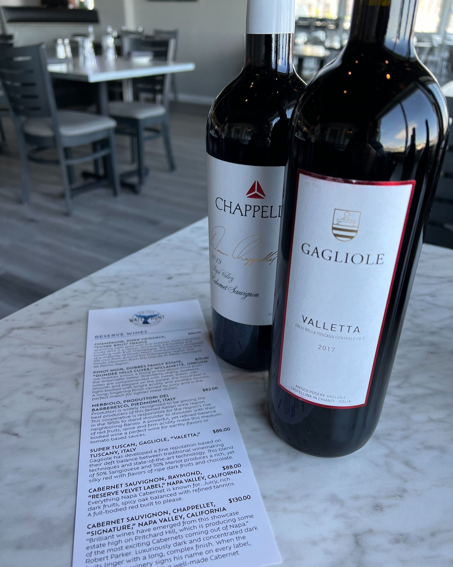 Two bottles of red wine and a receipt on a marble table in a restaurant setting.