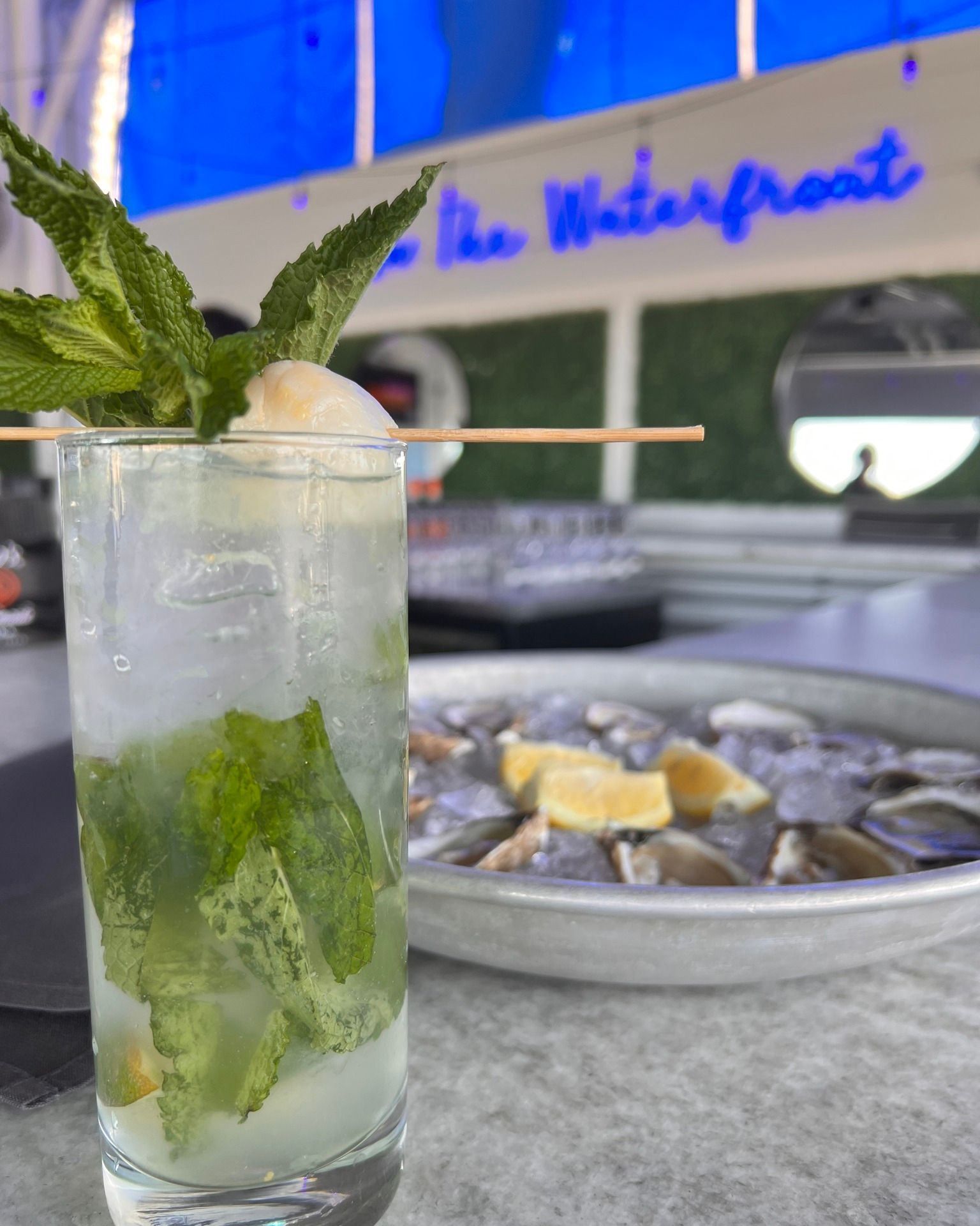 Tall cocktail with mint and lychee, with oysters on ice in the background.