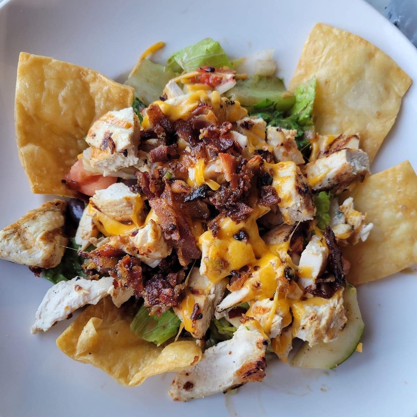 Chicken salad with bacon, cheese, and tortilla chips in a white bowl.