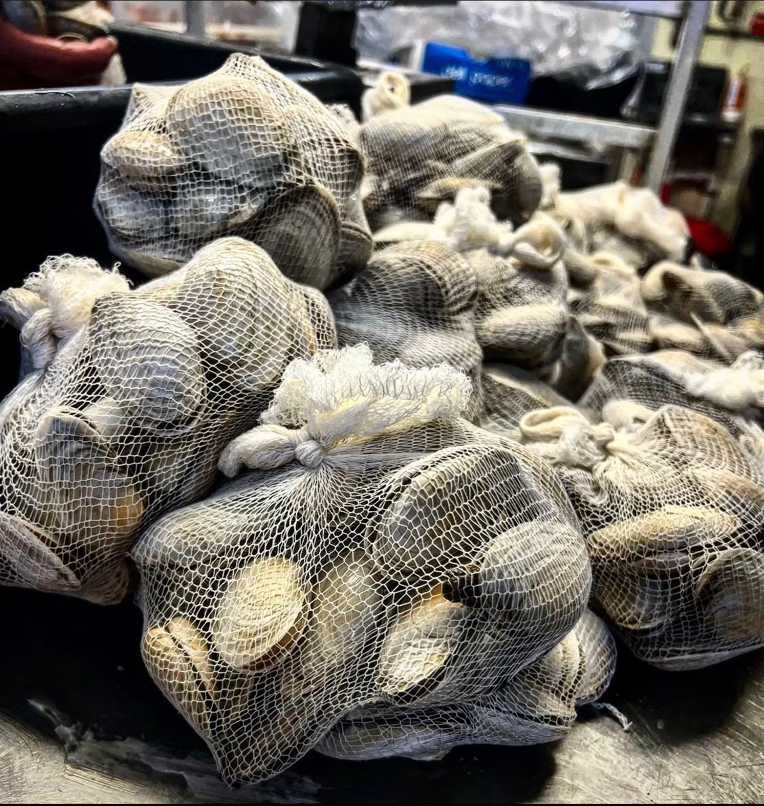 Bags of clams, wrapped in netting, piled together, possibly ready for sale or cooking.
