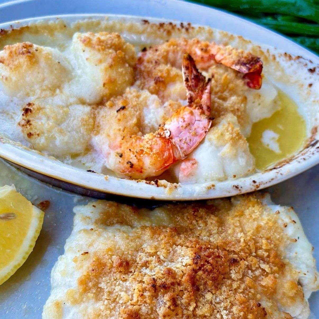 Seafood bake with shrimp and white fish topped with breadcrumbs. A lemon wedge is nearby.