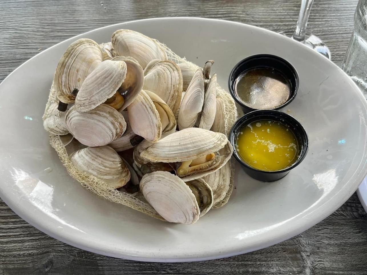 Steamed clams on a white plate with two small containers of butter and dipping sauce.