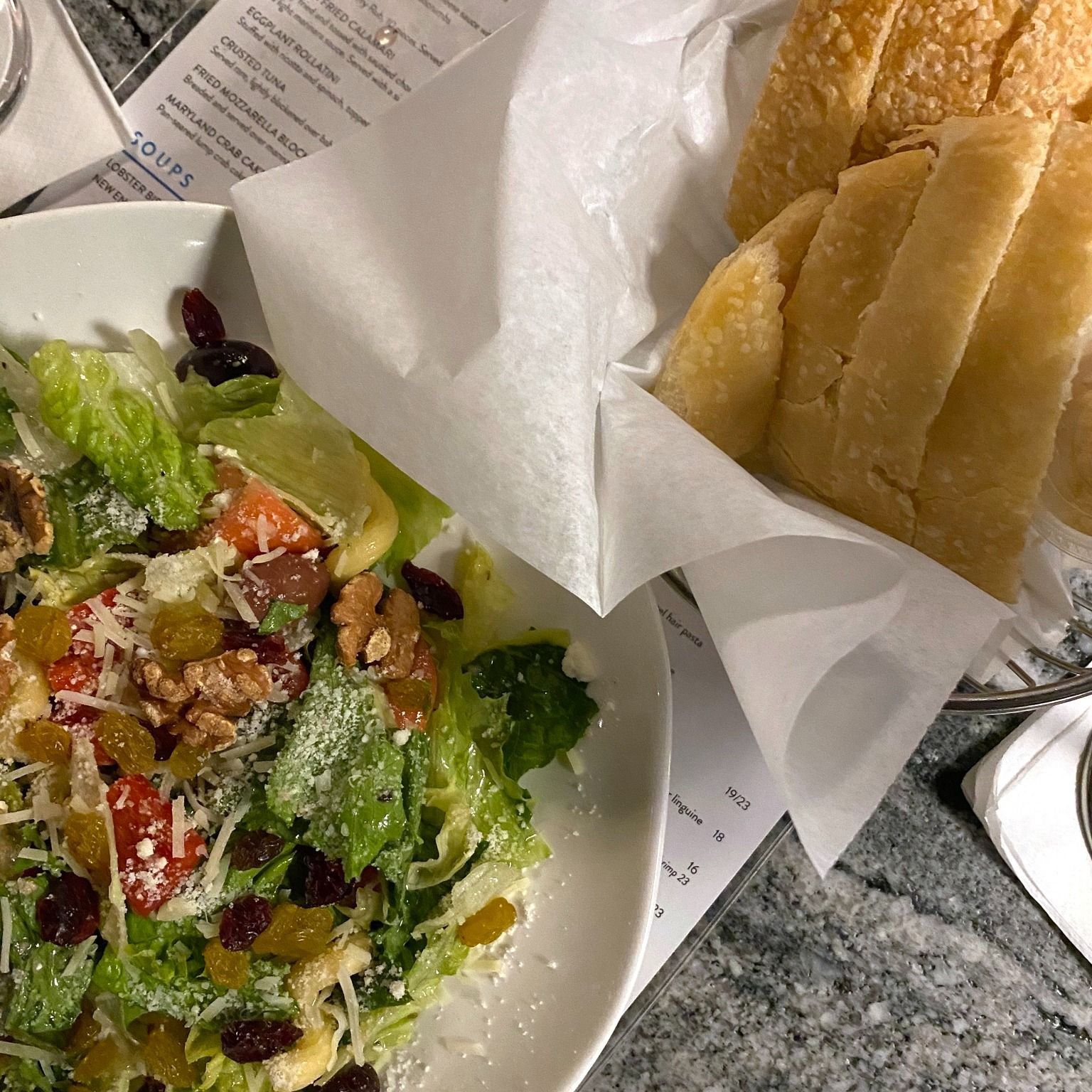 Salad with dried fruit and walnuts, next to bread in a basket.