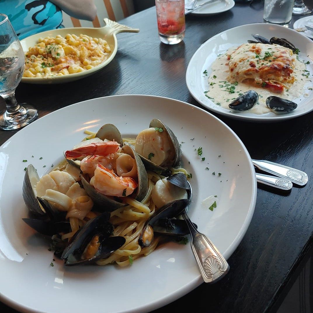 Plates of seafood pasta, lobster mac and cheese, and lasagna on a dark table at a restaurant.