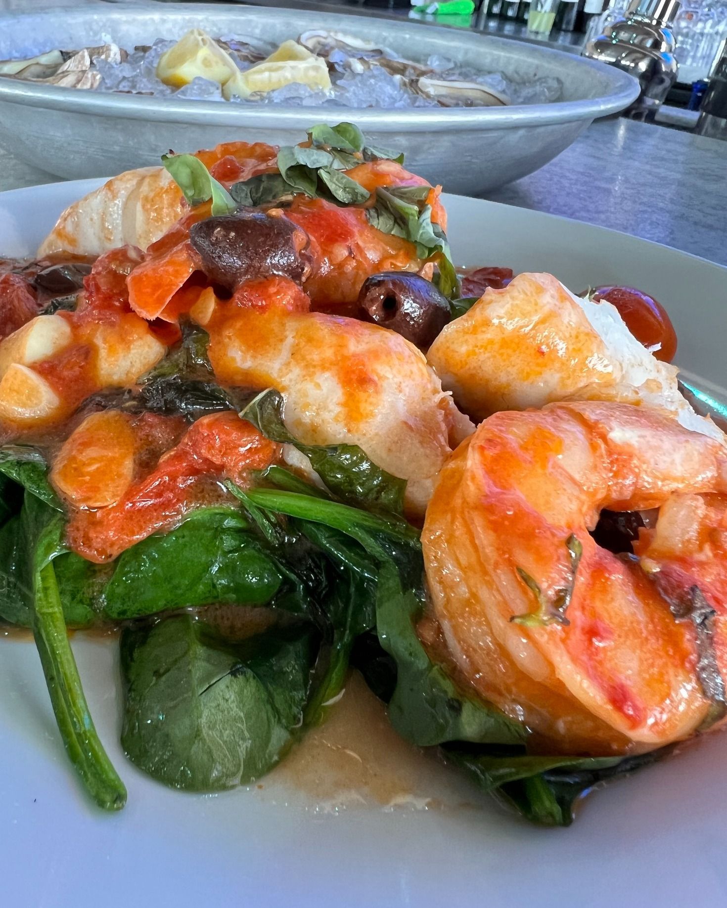 Shrimp and spinach dish in tomato sauce, with olives, on a white plate.