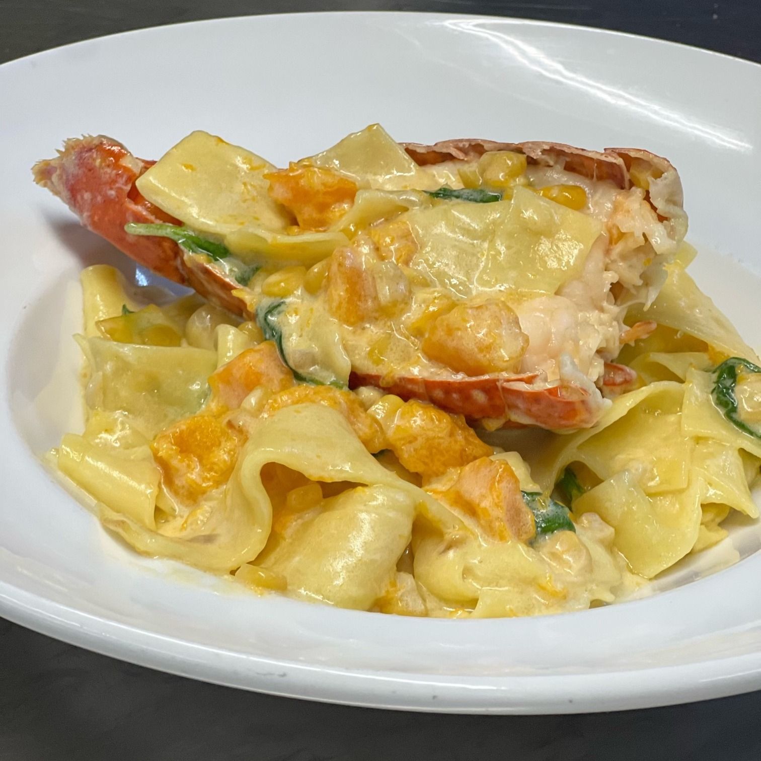 Lobster pasta in a white bowl, with creamy sauce, yellow pasta, and a lobster tail on top.