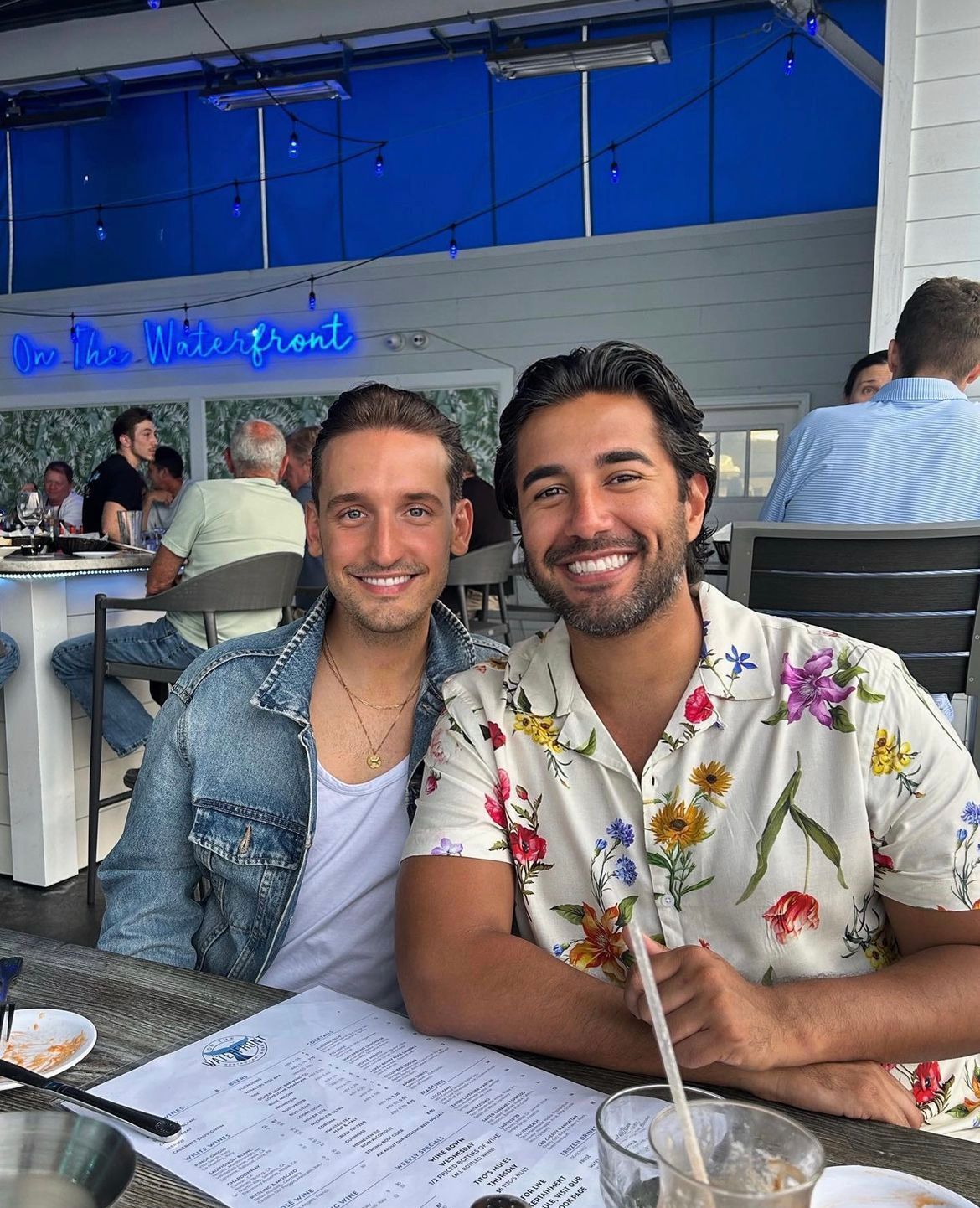 Two smiling people pose at a waterfront restaurant.