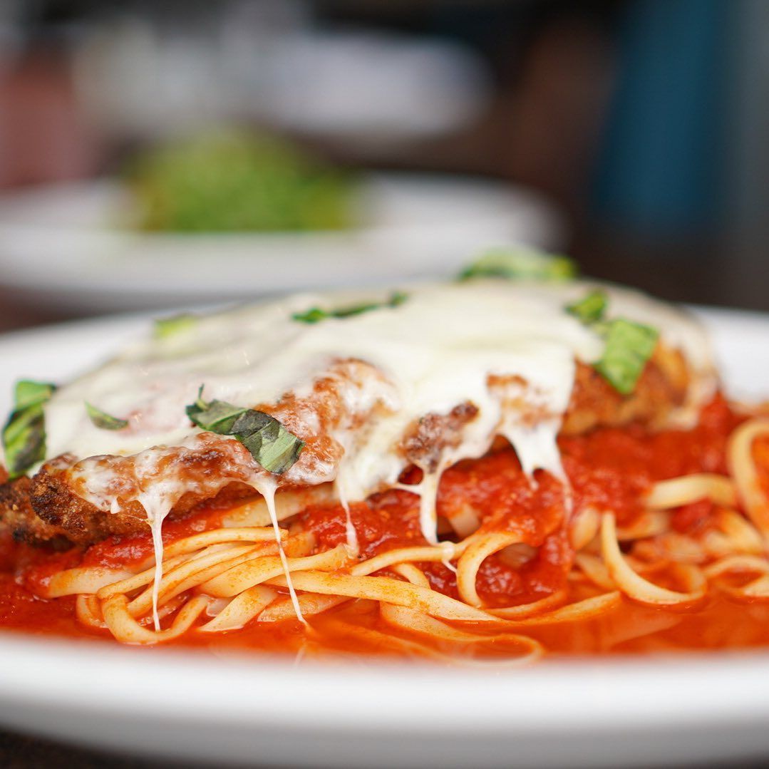 Chicken parmesan with melted cheese and basil over linguine in tomato sauce.