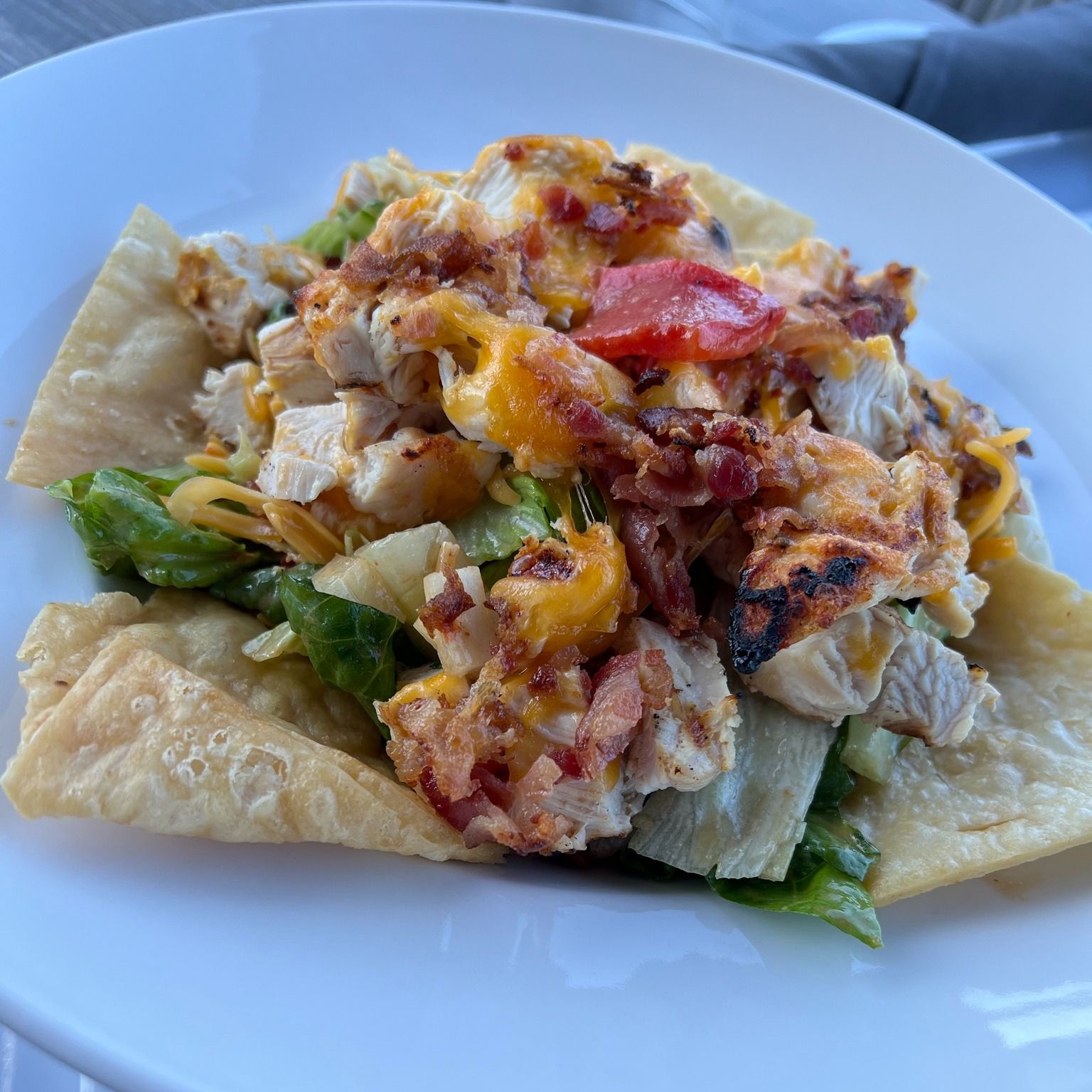 Chicken salad on a fried tortilla, topped with melted cheese, bacon, and a tomato.