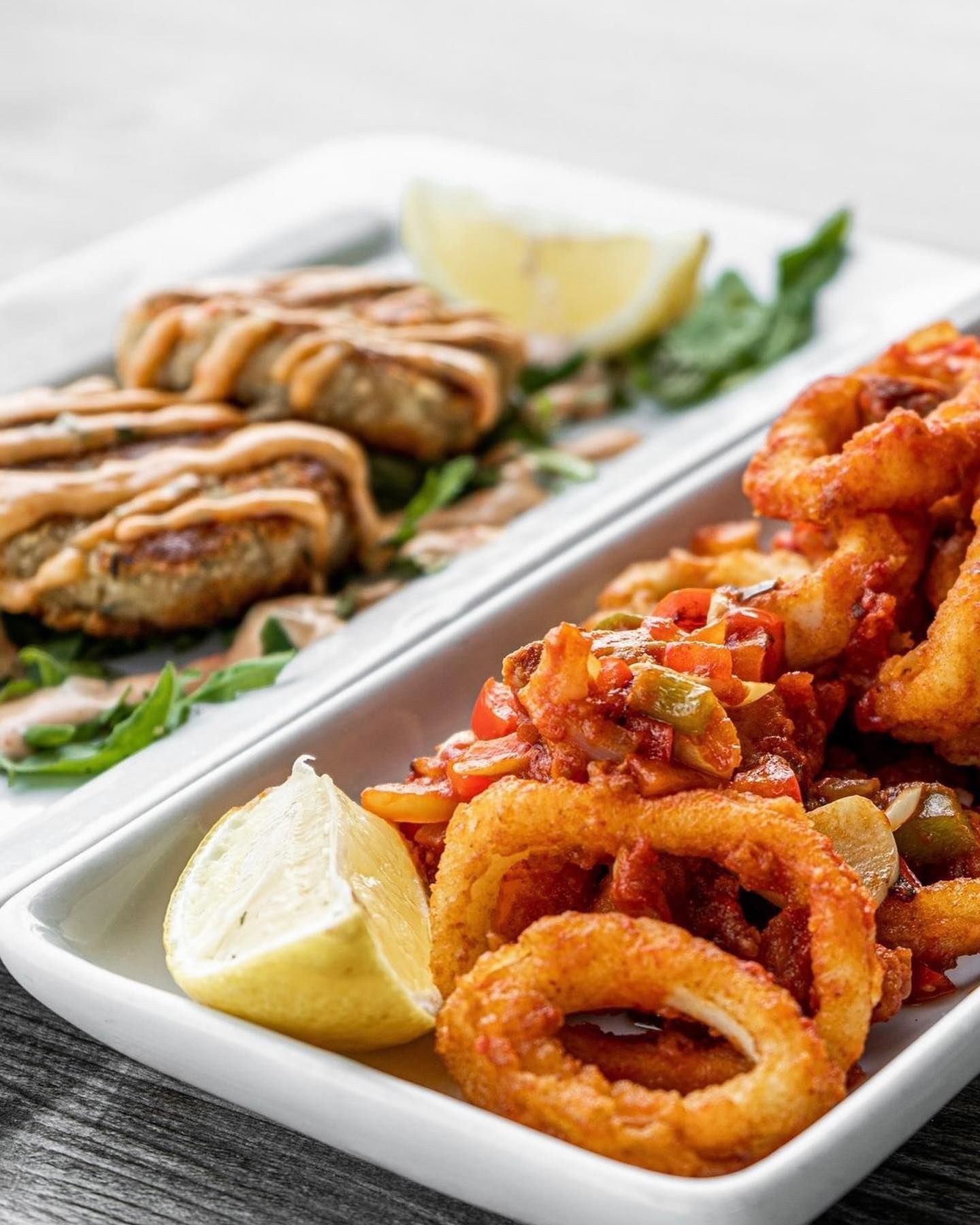Fried calamari and crab cakes on a white plate with lemon wedges.