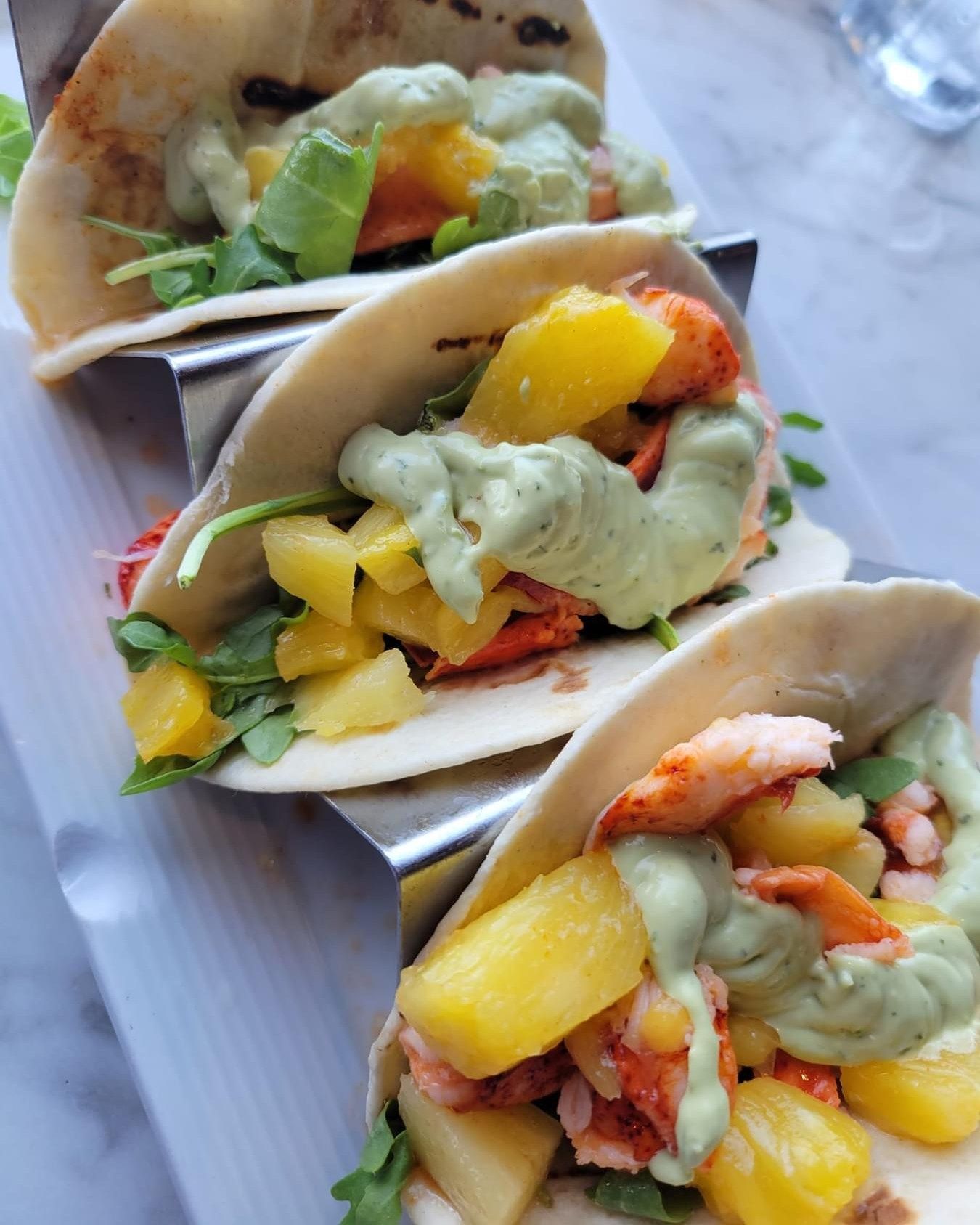 Lobster tacos with mango and avocado crema on a metal stand.