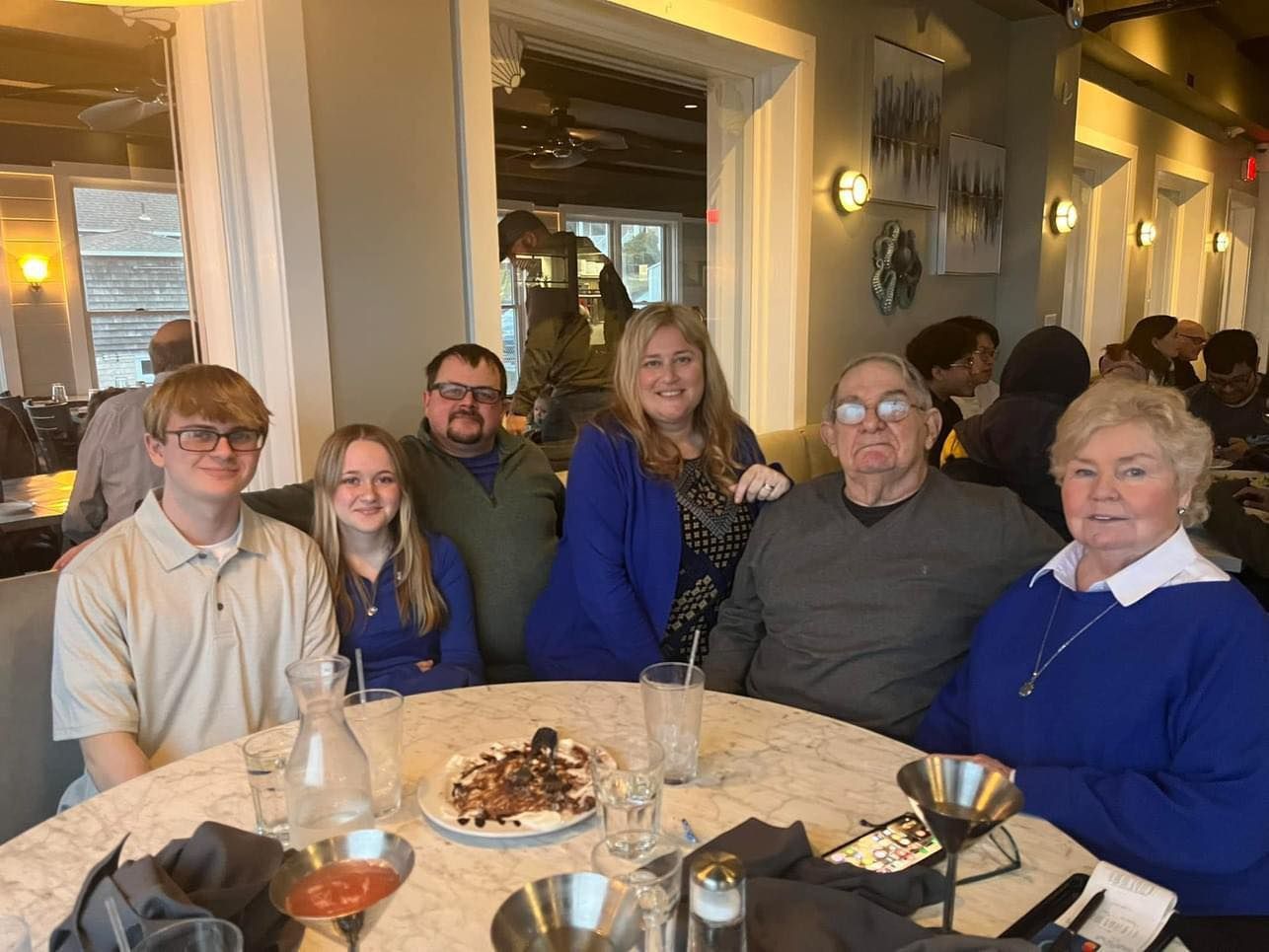 Group of people at a restaurant, seated at a table with food, smiling.