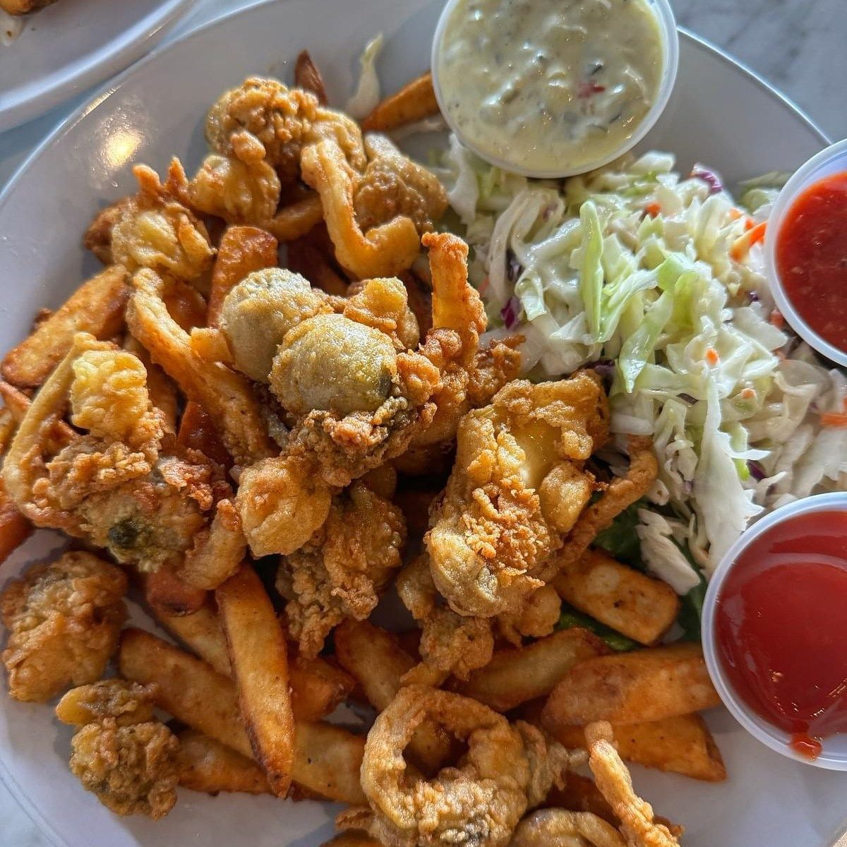 Fried seafood platter with fries, coleslaw, tartar sauce, and ketchup.