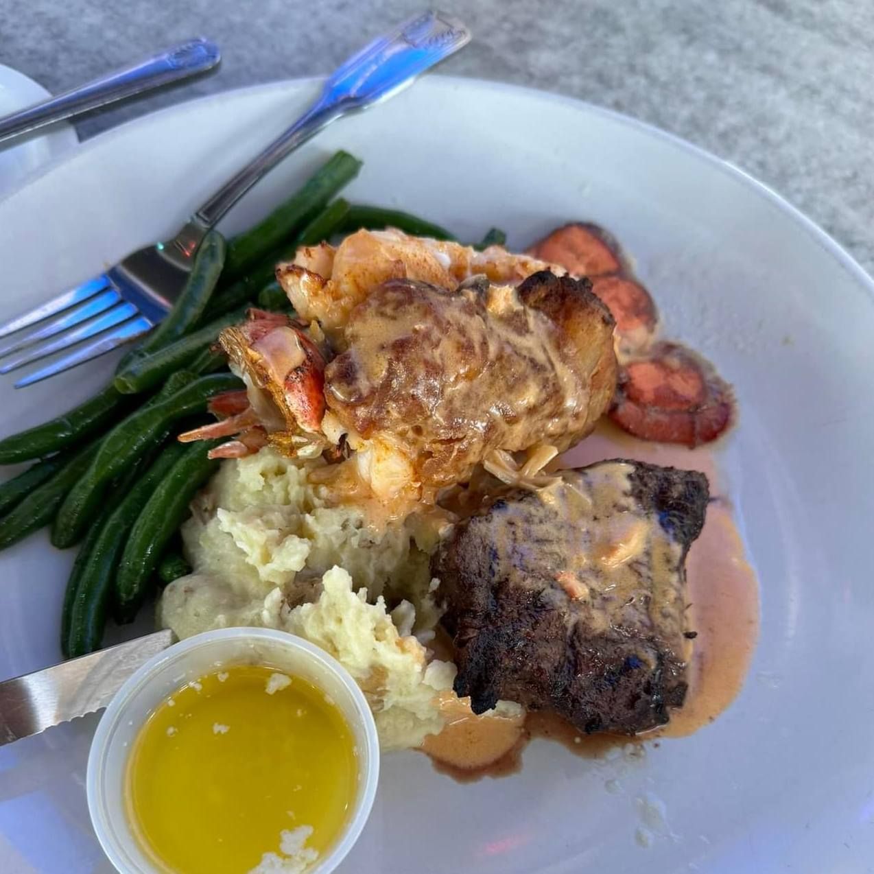 Lobster, steak, mashed potatoes, green beans, and butter.