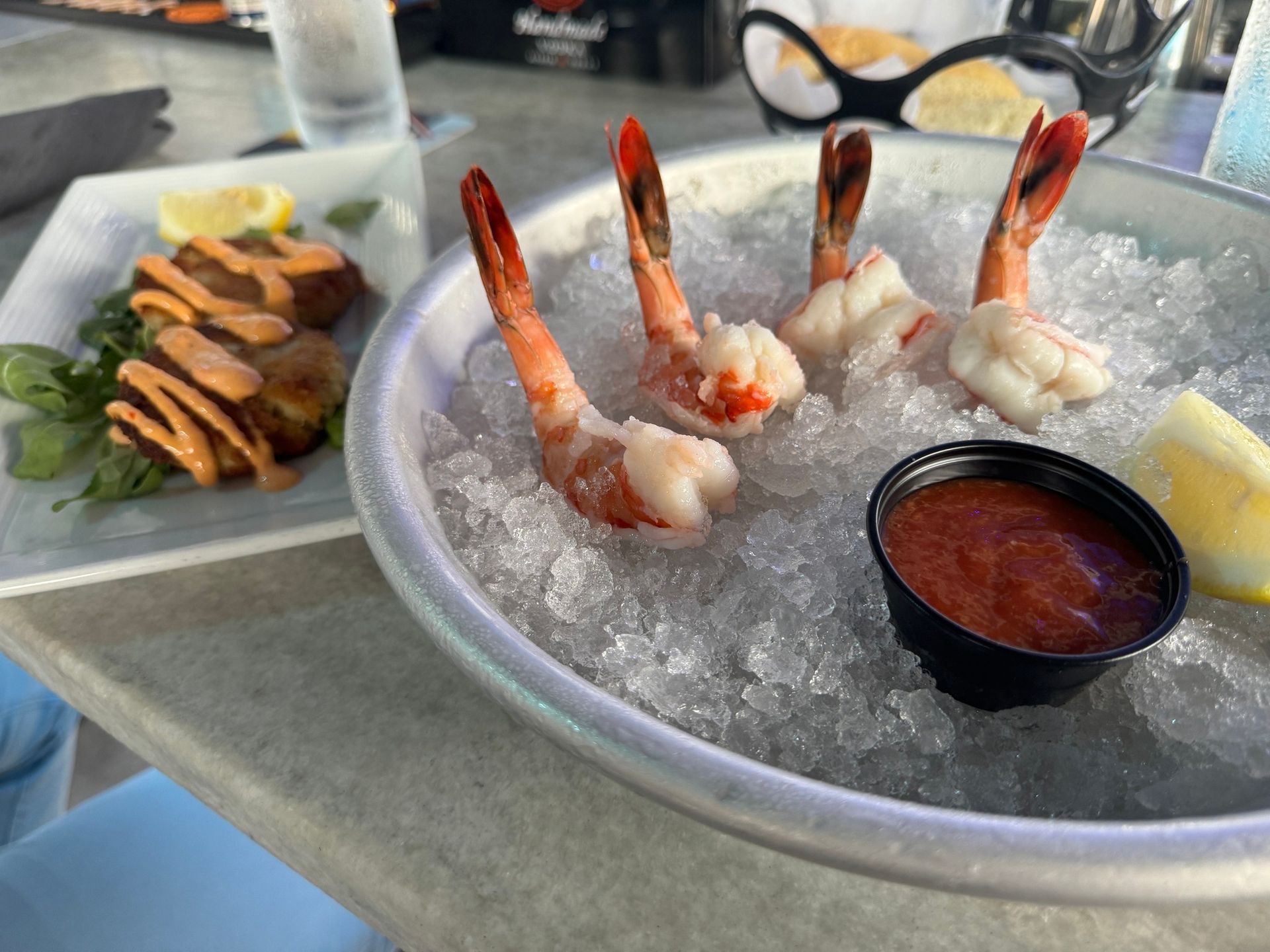 Shrimp cocktail with red sauce, served on ice, with fried dish on the side. Outdoors on a table.