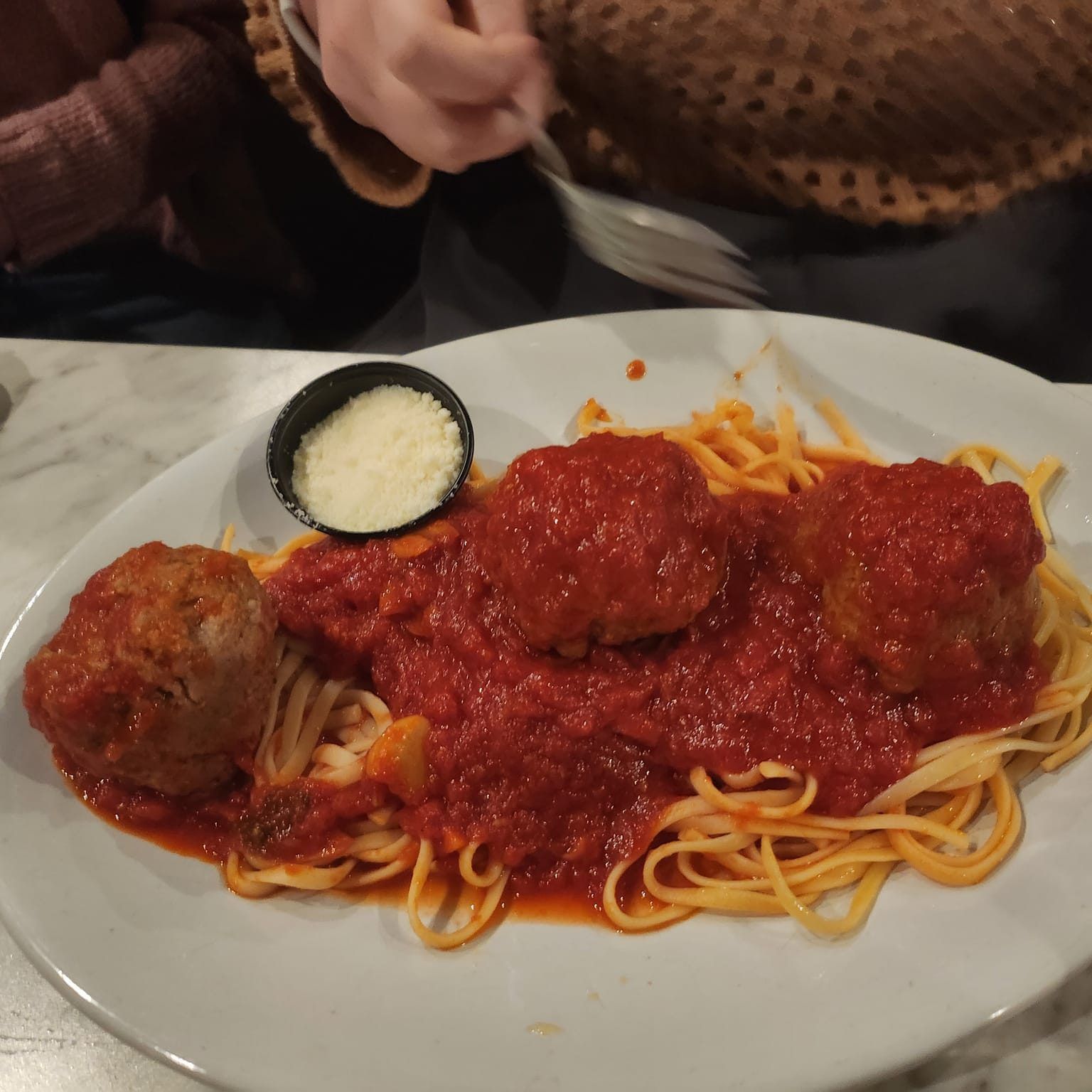 Spaghetti and meatballs with tomato sauce and a side of grated cheese on a white plate.