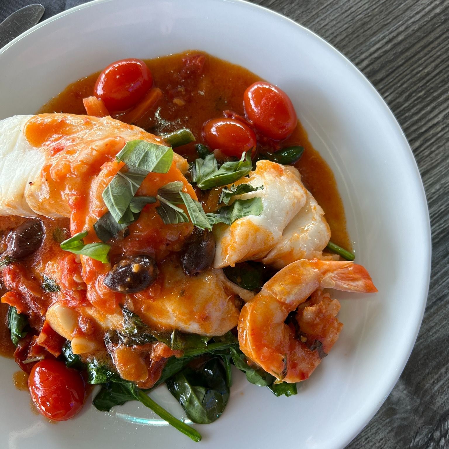 Fish and shrimp with tomatoes, spinach, olives, and basil in a tomato sauce.
