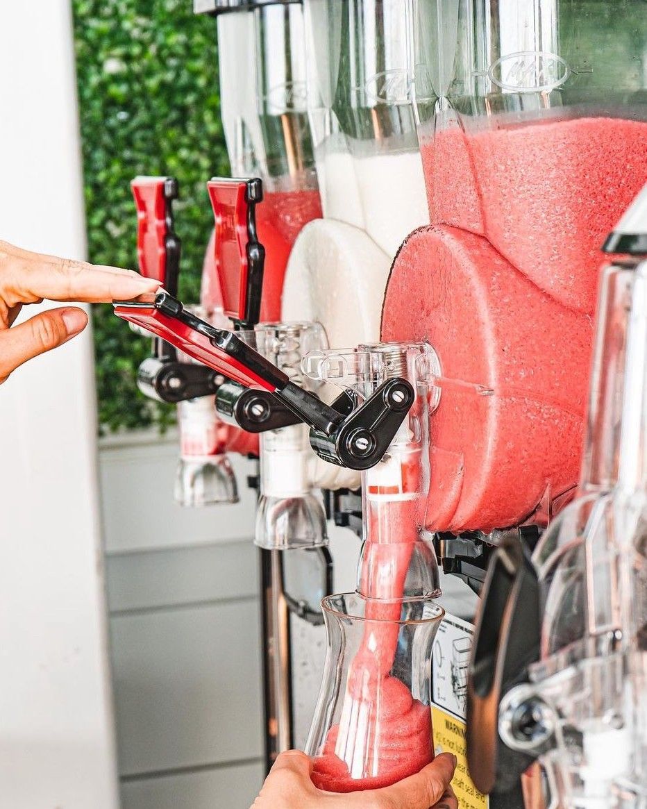 Hand dispensing red slush from a multi-flavor frozen beverage machine.