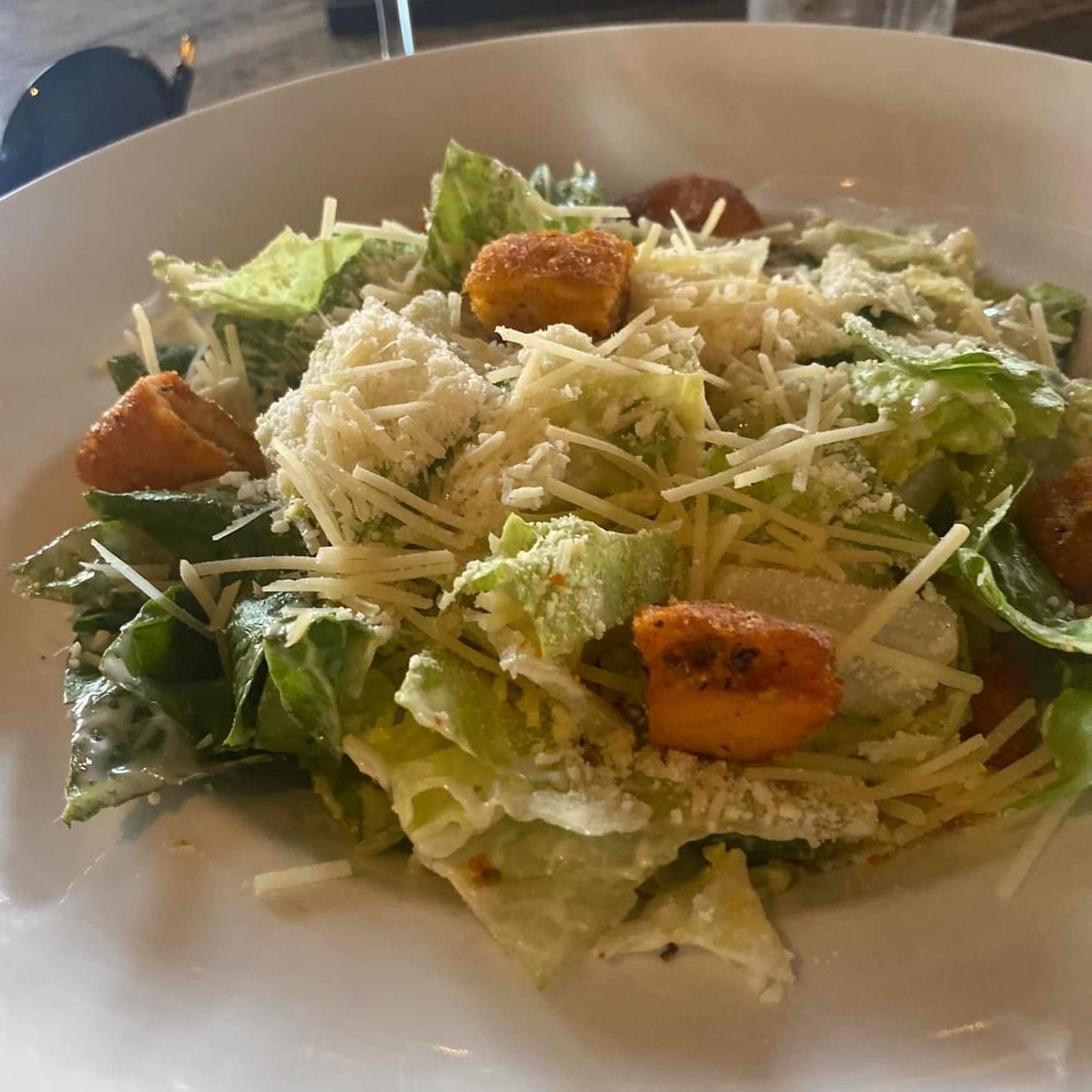 Caesar salad with romaine lettuce, croutons, and shredded parmesan cheese in a white bowl.