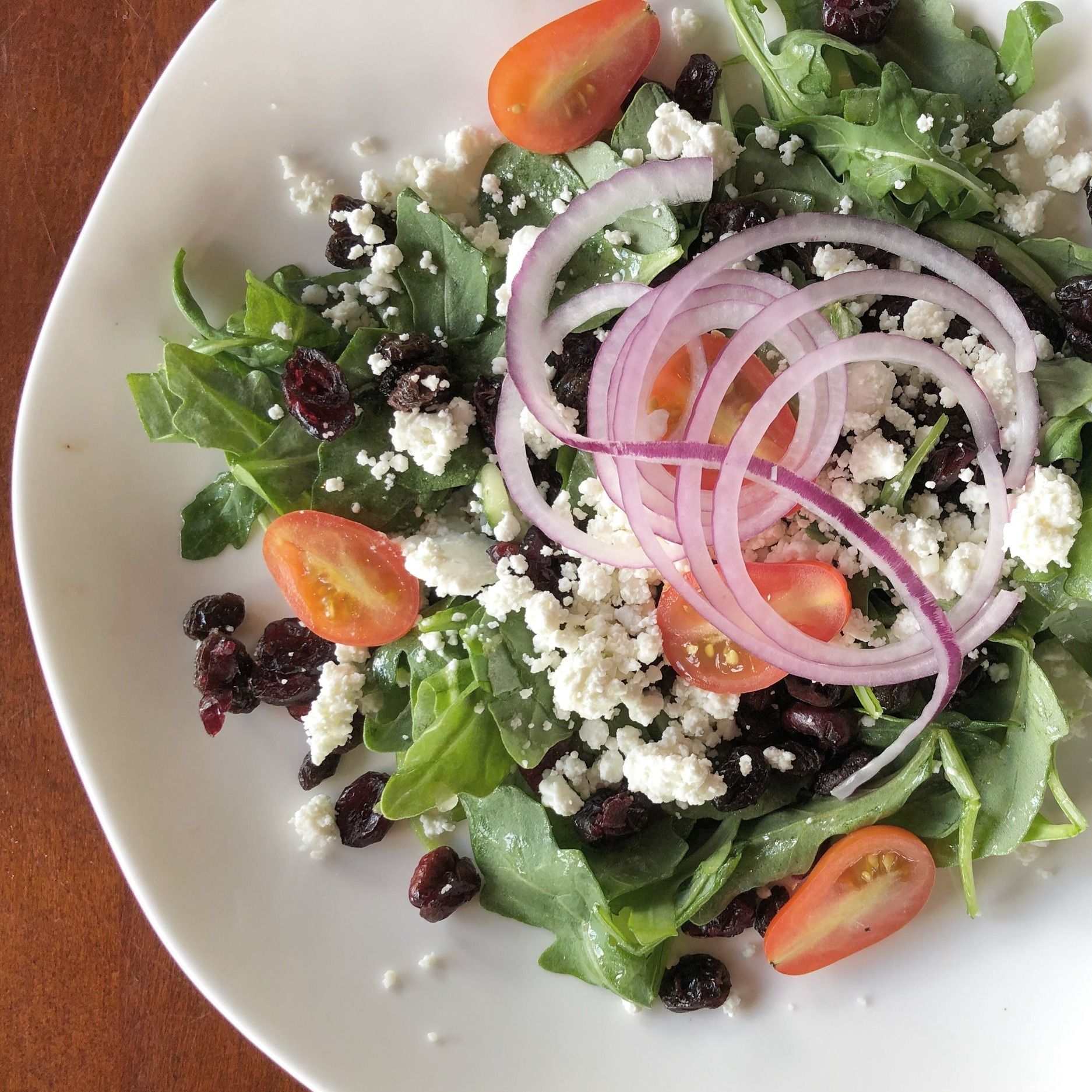 Salad with arugula, red onion, cherry tomatoes, cranberries, and feta cheese on a white plate.