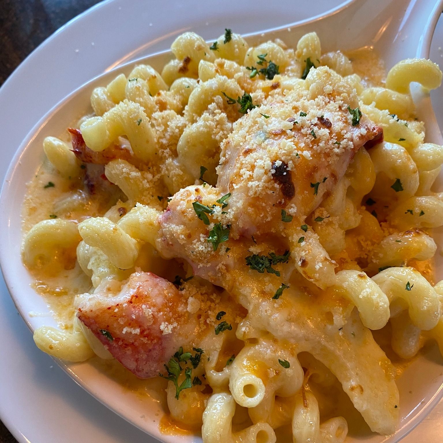 Lobster mac and cheese in a white dish, garnished with parsley and breadcrumbs.