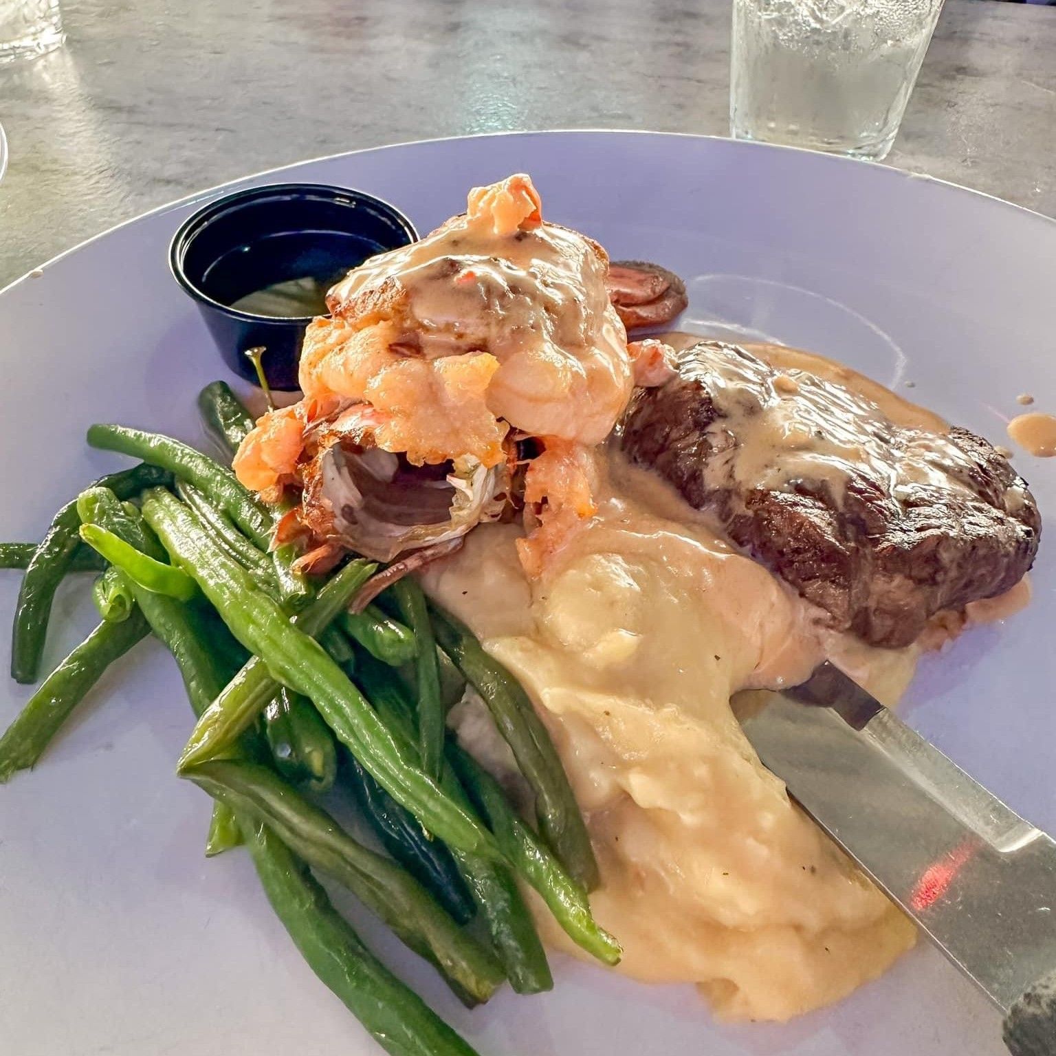 Steak and lobster dish on a white plate with green beans and mashed potatoes.