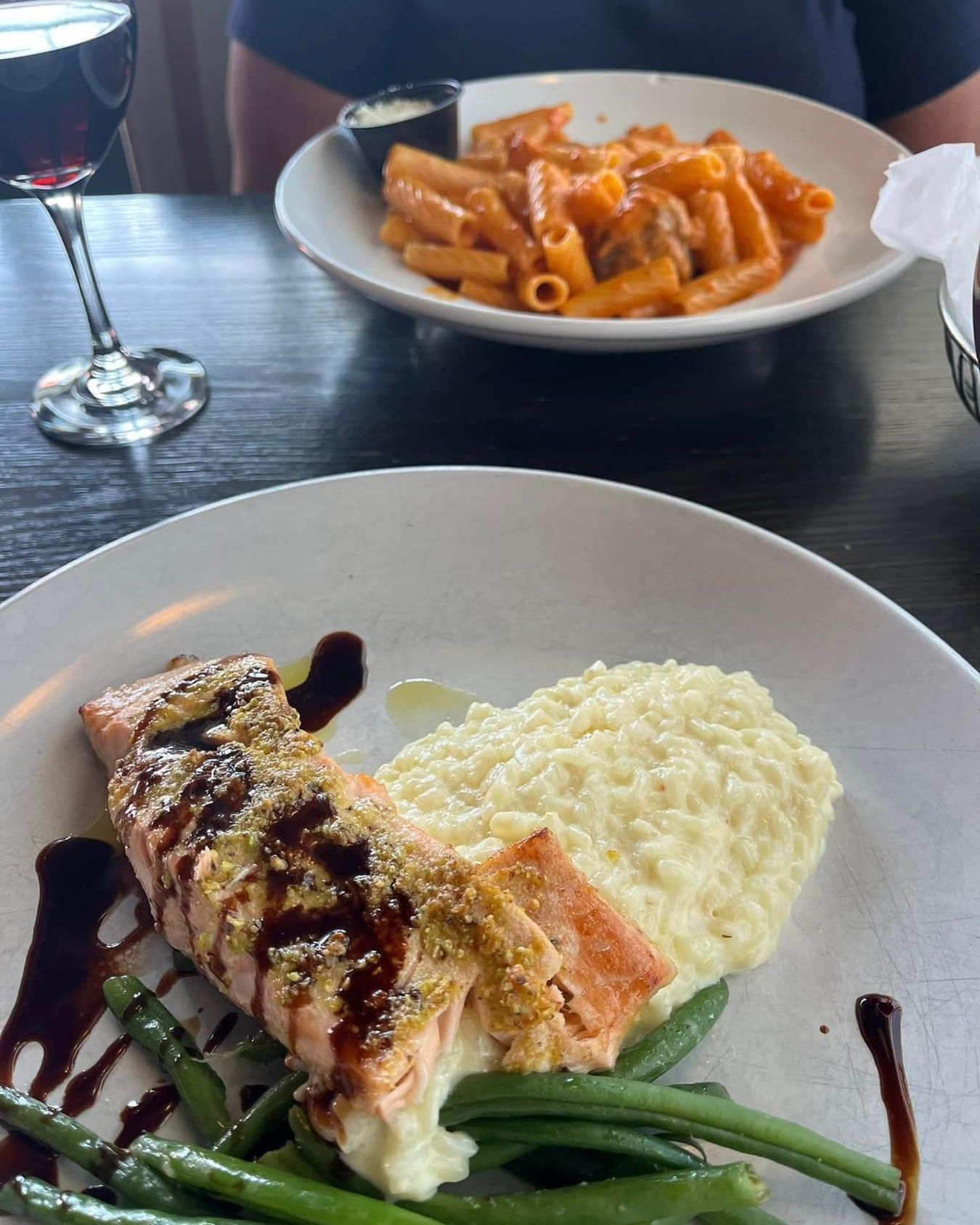 Salmon with risotto and green beans, pasta dish, glass of red wine on a dark table.