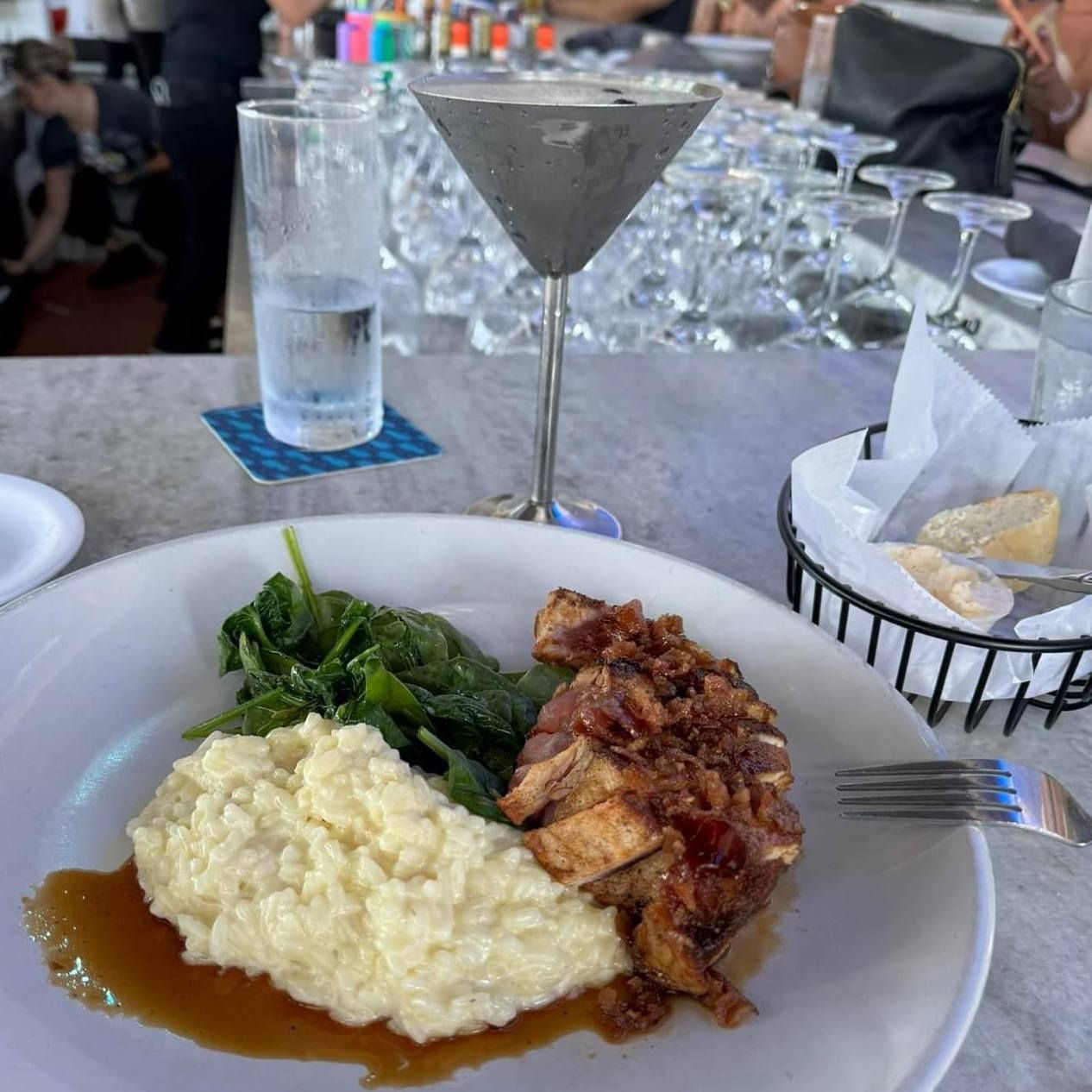 Plate of food with spinach, mashed potatoes, and meat, next to a martini and water glass at a bar.