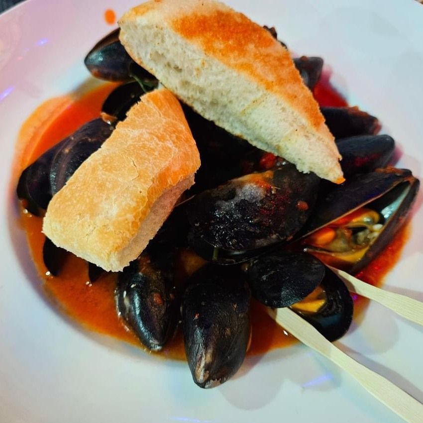 Mussels in a red sauce with bread on a white plate.