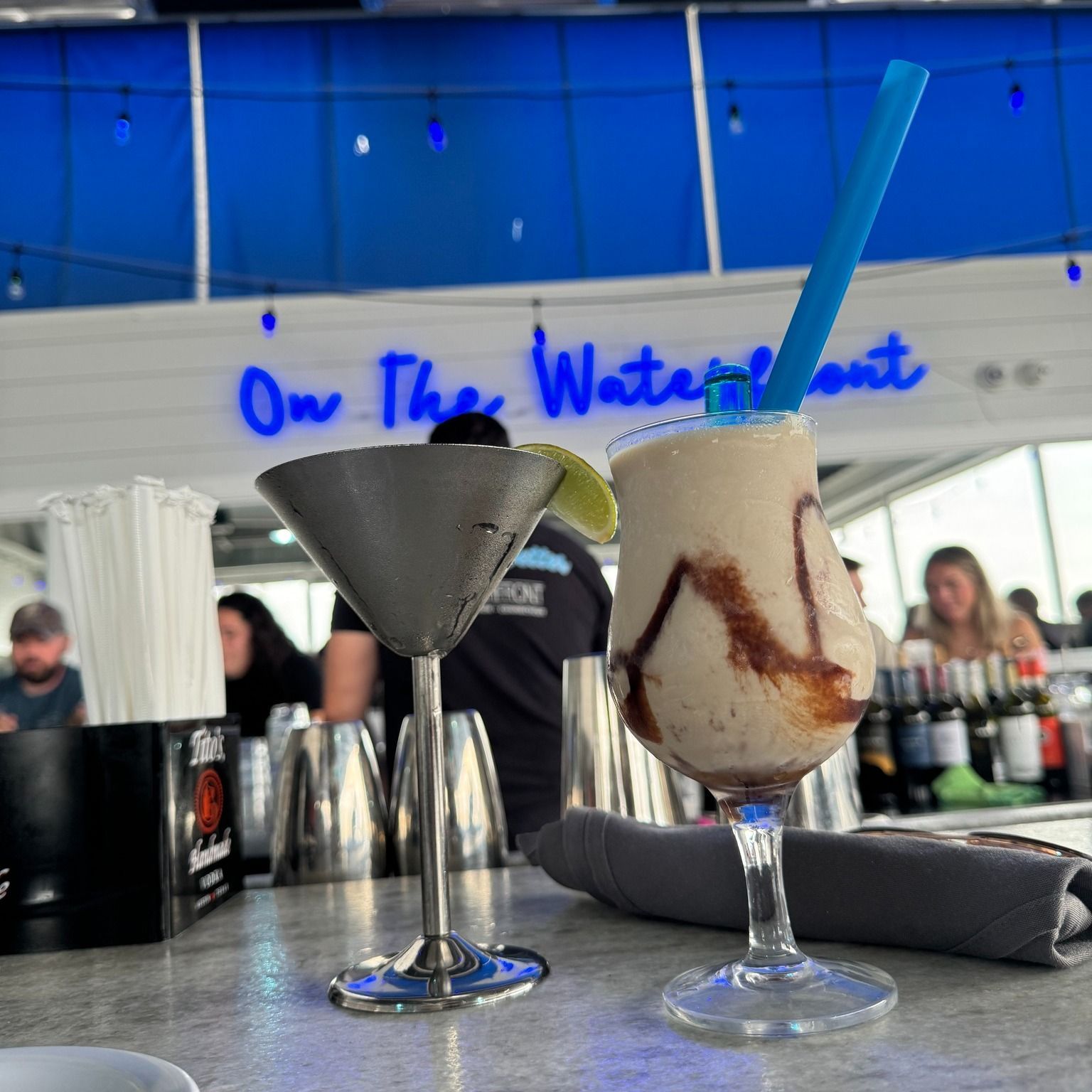 One in a silver martini glass with a lime, another in a clear glass with a blue straw and chocolate swirls.