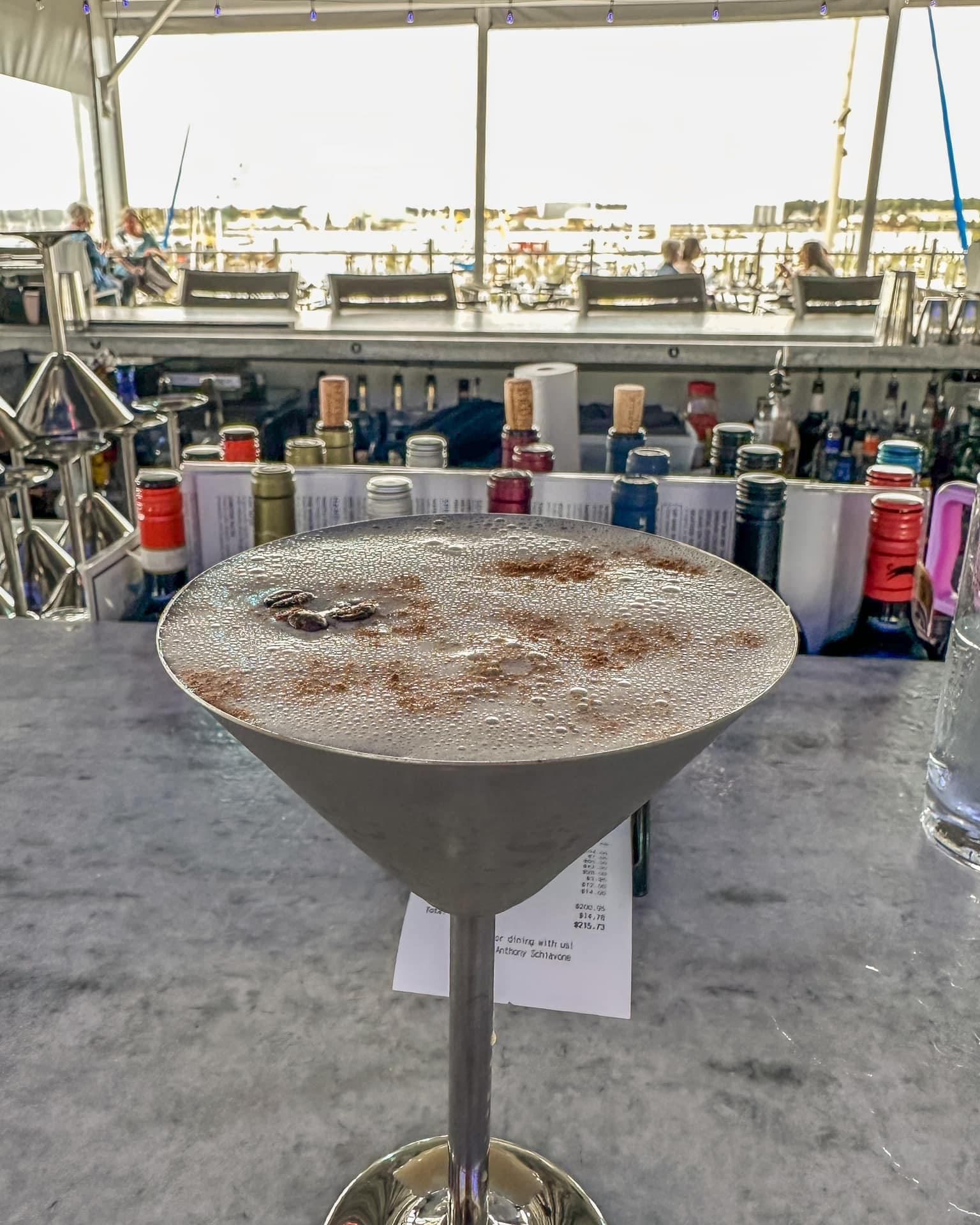 Martini glass with a foamy, cocoa-dusted drink on a bar.