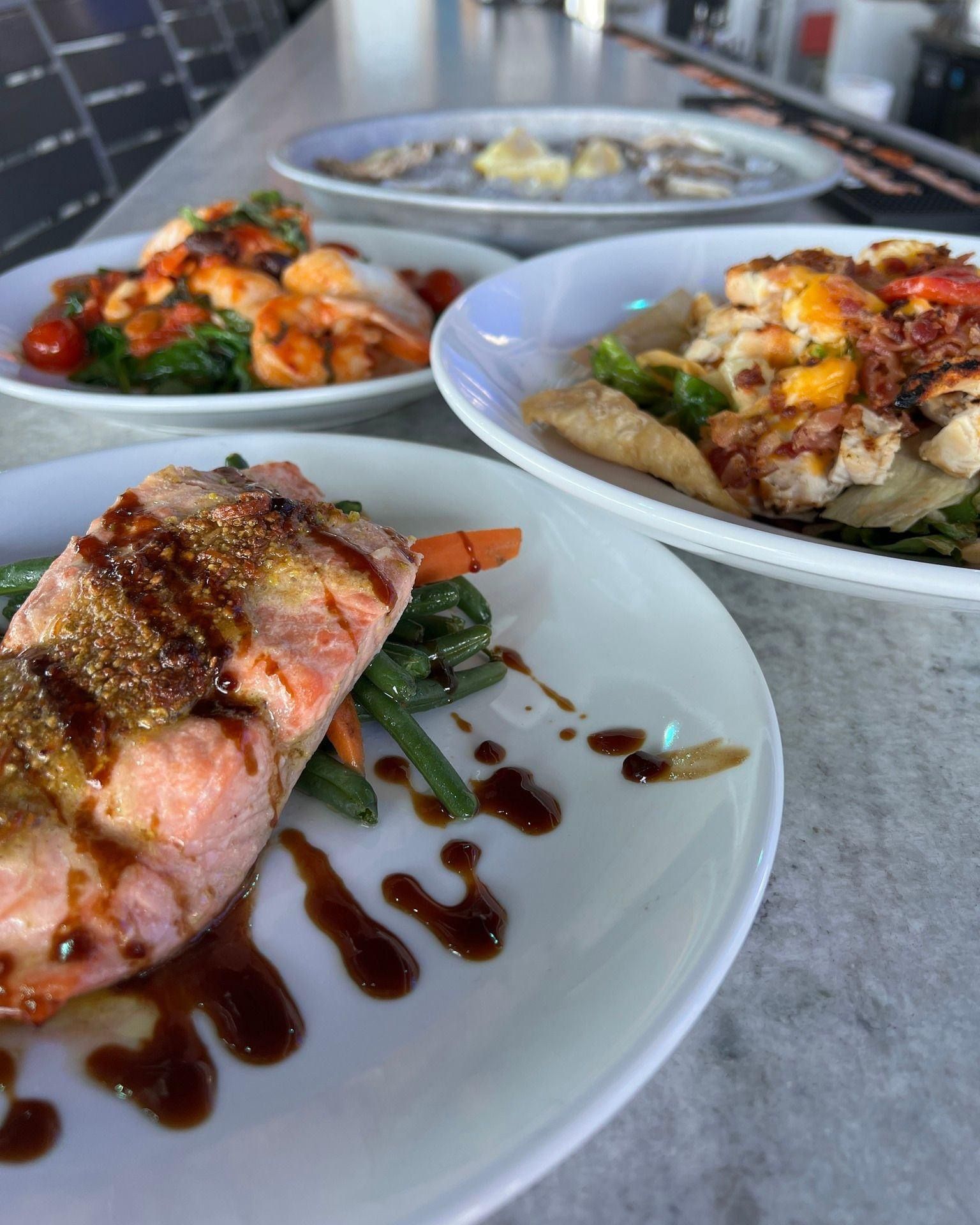 Plated seafood dishes, including salmon and shrimp, on a light-colored surface.