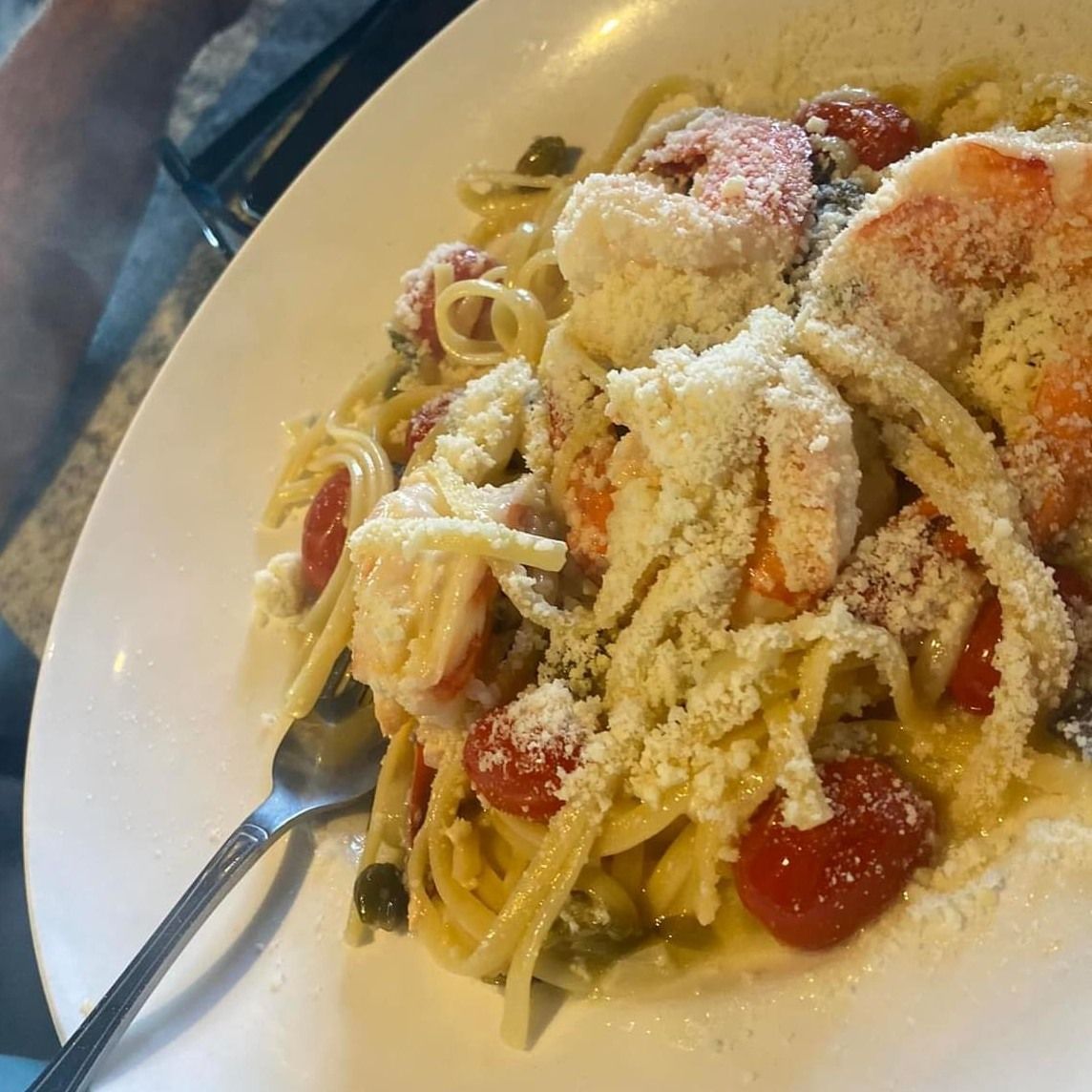 Linguine pasta with shrimp, cherry tomatoes, capers, and Parmesan cheese on a white plate.