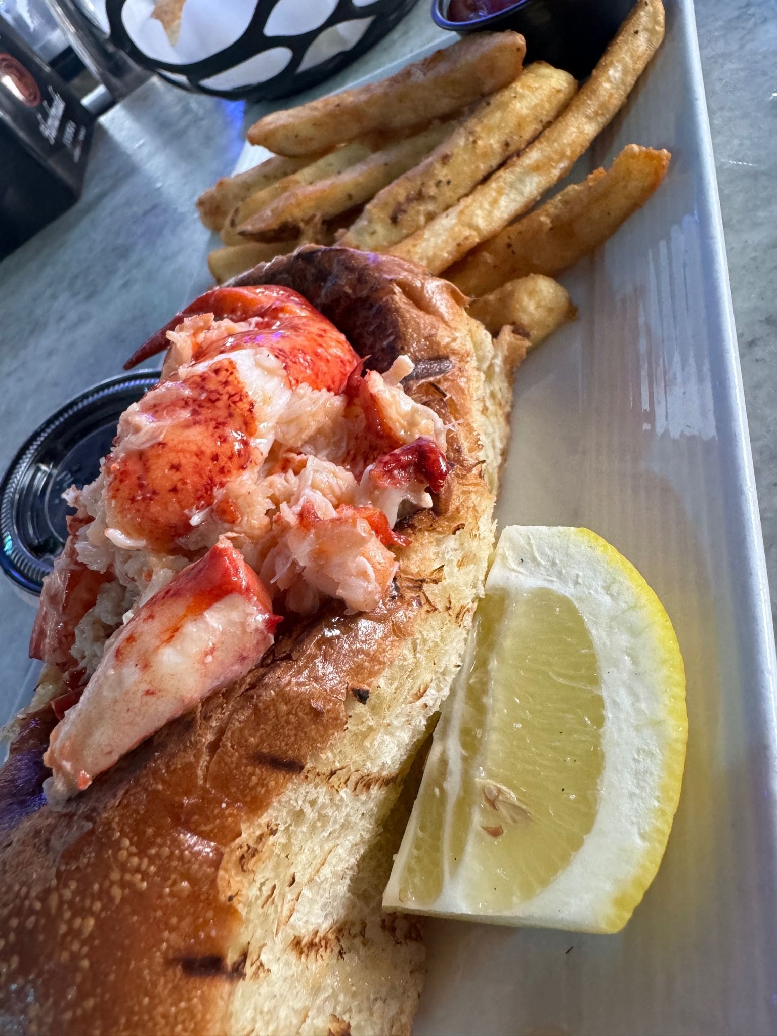 Lobster roll with fries and a lemon wedge on a white plate.