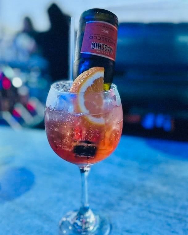 Cocktail in a stemmed glass with orange slice, ice, and Prosecco bottle.