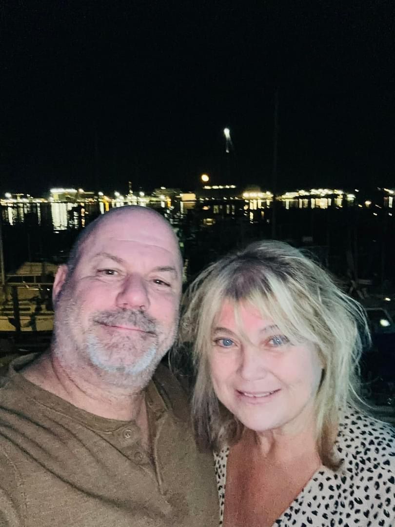 Couple smiling at the camera, night scene with city lights and a firework.