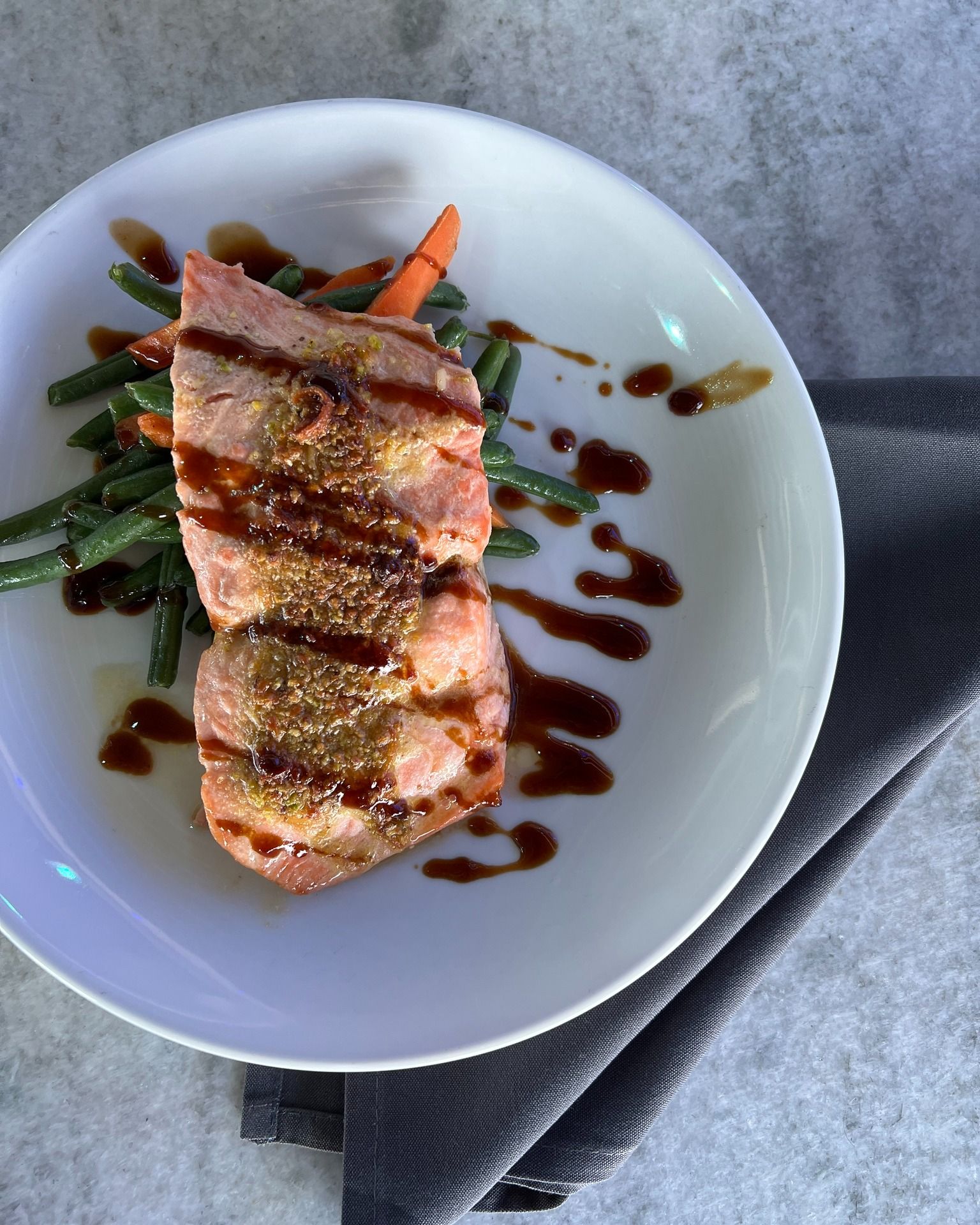 Seared tuna with green beans and carrots, drizzled with sauce on a white plate.