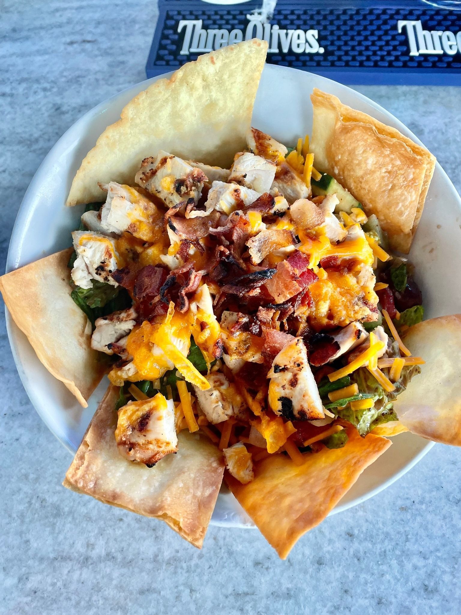 Chicken salad with tortilla chips, cheese, and bacon in a white bowl.