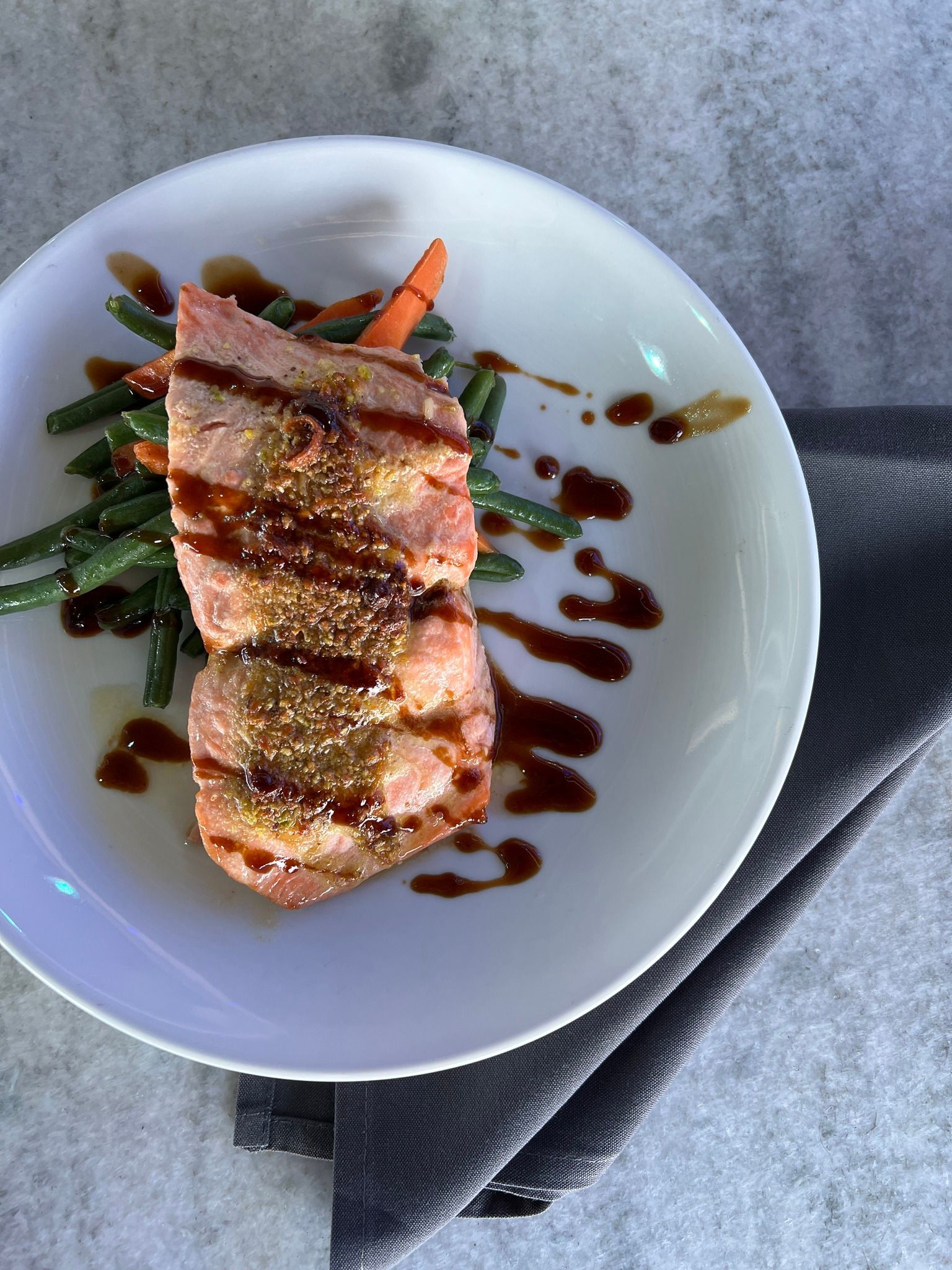 Plate with seared tuna, green beans, carrots, and drizzle of sauce. Grey napkin.