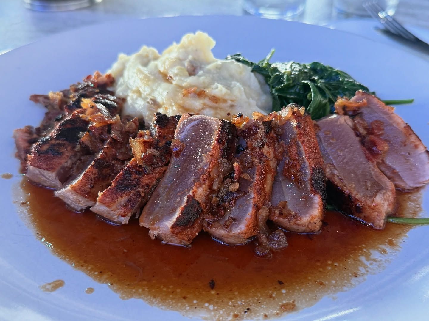 Seared tuna steak with mashed potatoes and sauteed spinach on a white plate.