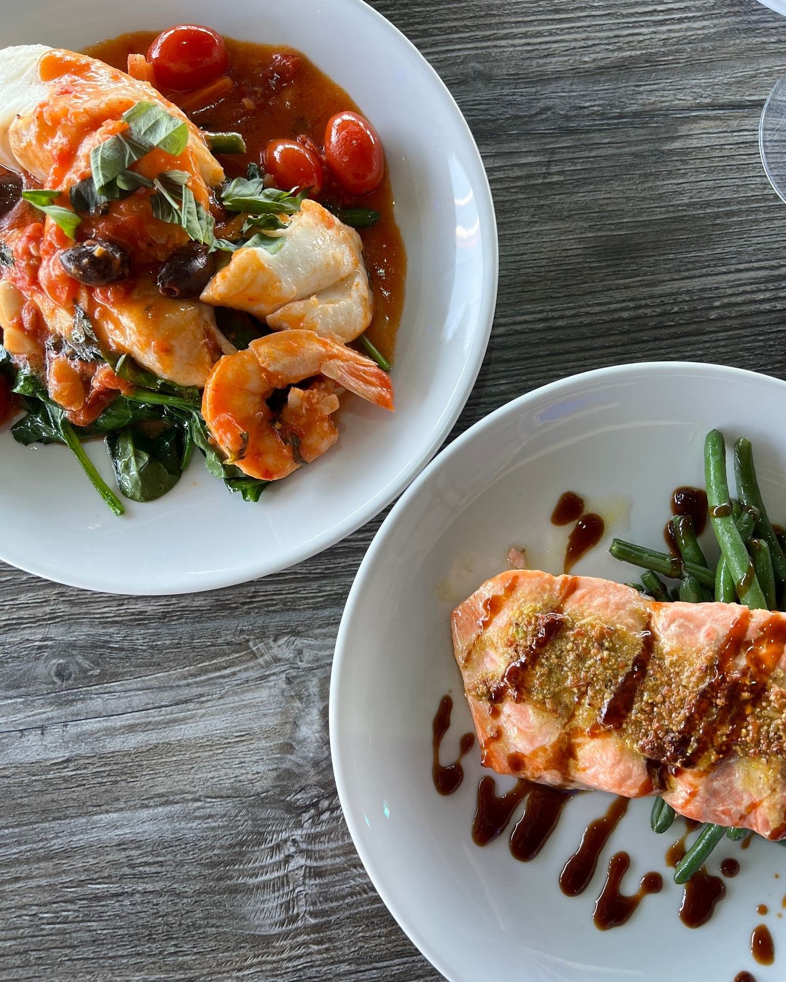 Two plates of seafood: fish with tomatoes and shrimp.