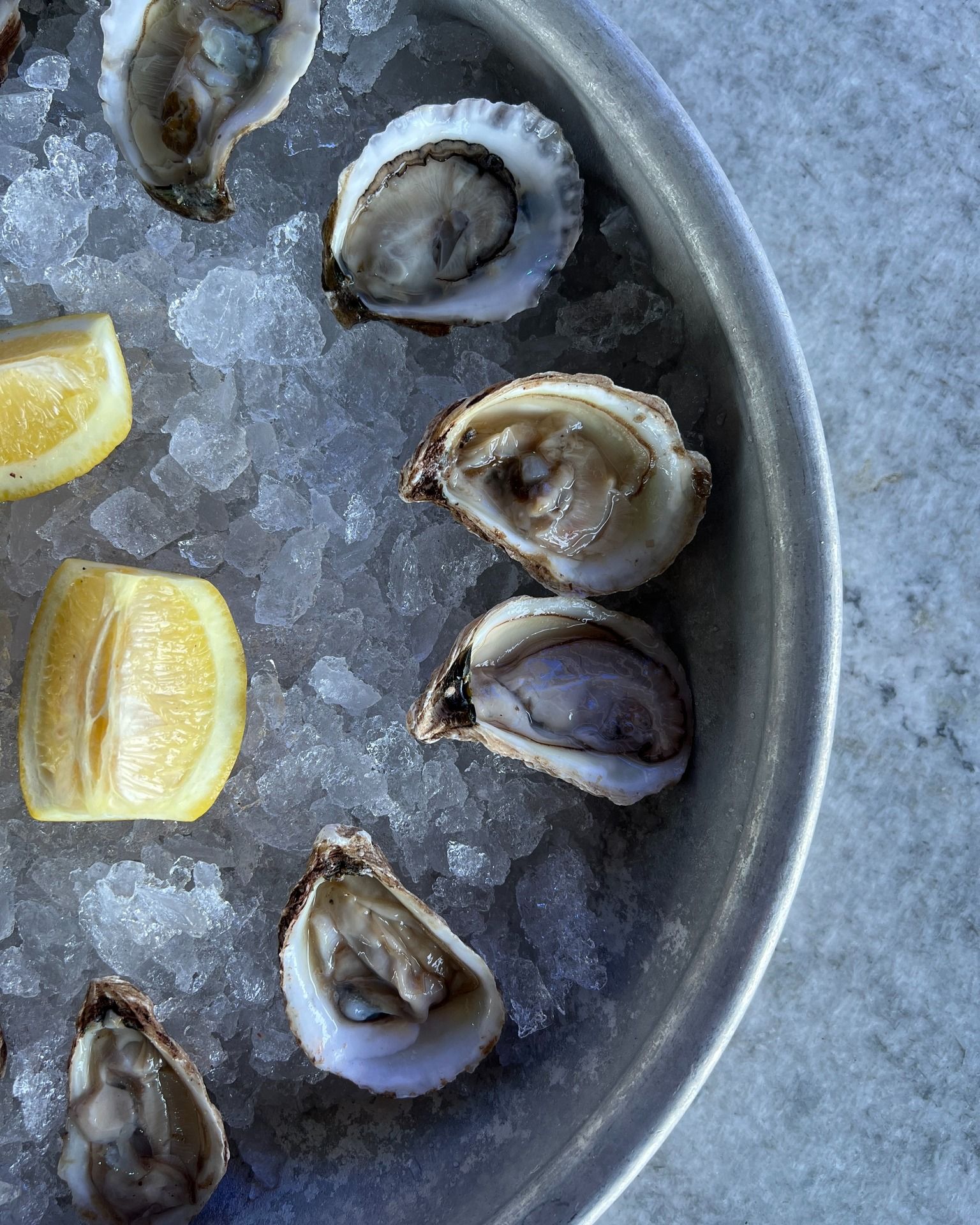Oysters on ice in a metal tray with lemon wedges.