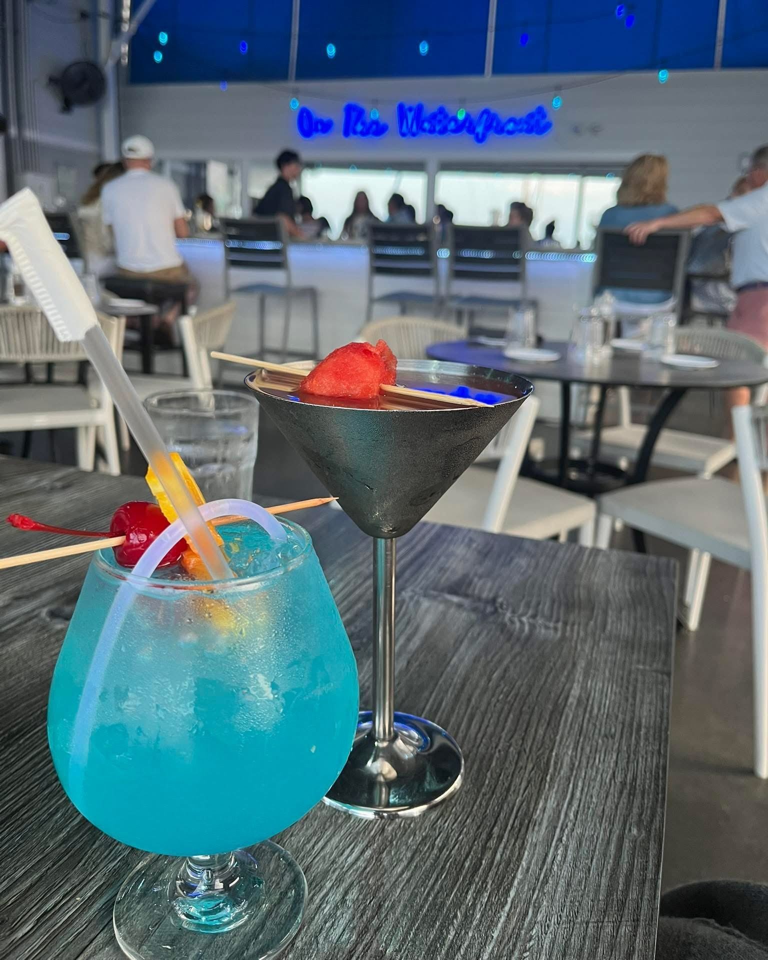 Two colorful cocktails on a wooden table at an outdoor bar.