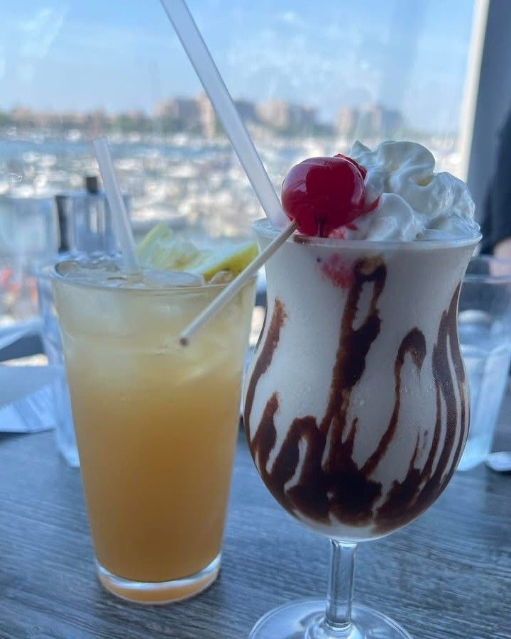 One yellow drink with pineapple and one dessert-like drink with chocolate syrup, whipped cream, and cherry.