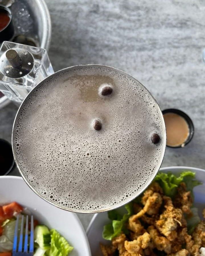 Cocktail with three coffee beans on top, surrounded by food, on a restaurant table.