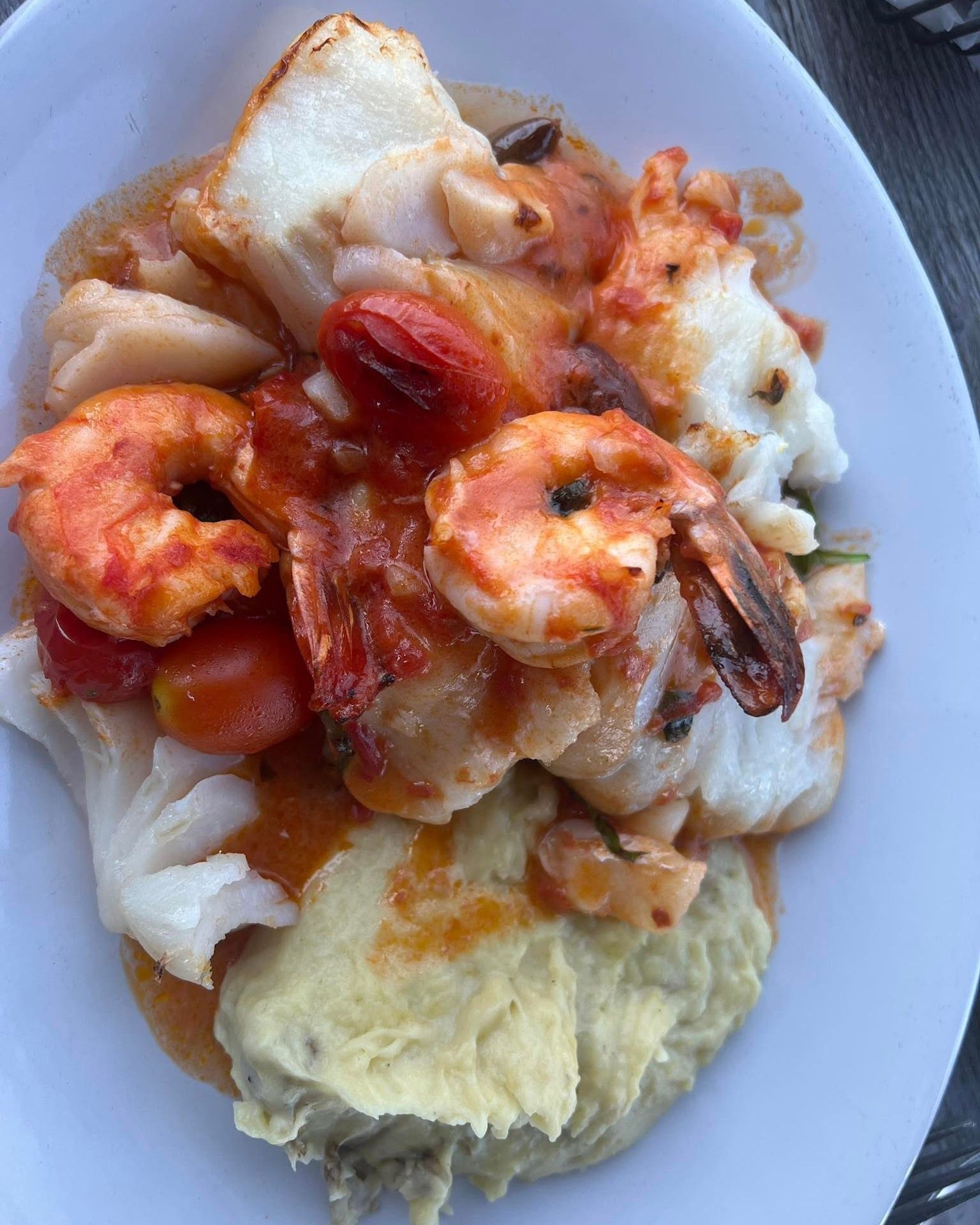 Seafood dish with shrimp, white fish, and sauce over mashed potatoes.
