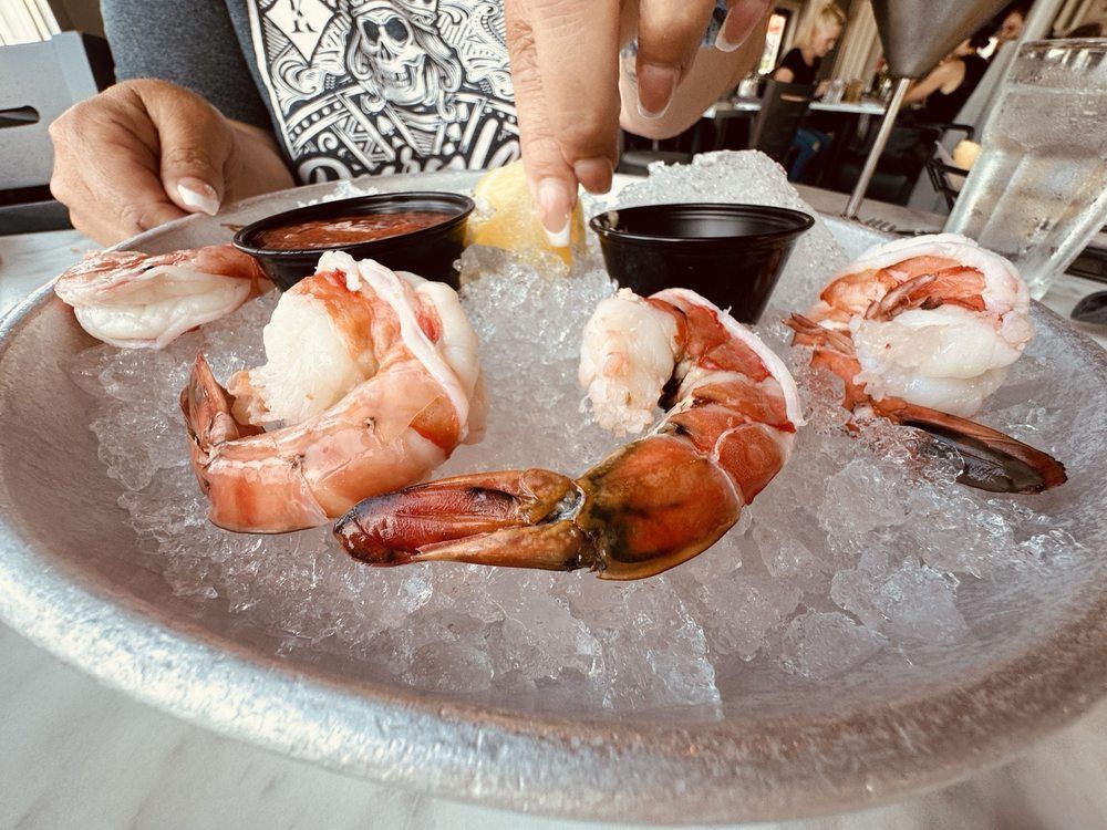 Shrimp cocktail on ice, with dipping sauces and a lemon wedge. A hand reaches for a shrimp.