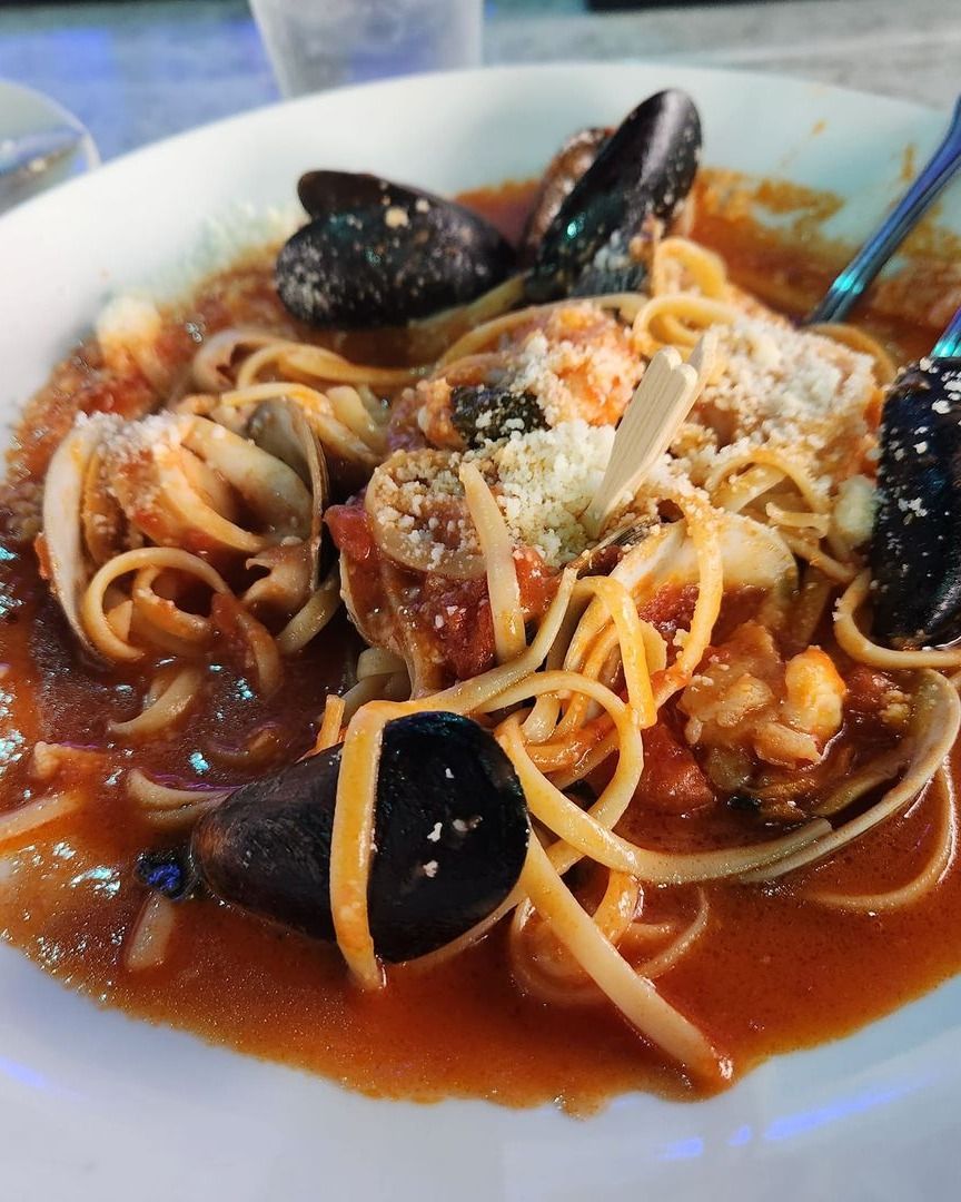 Plate of linguine with mussels, clams, and tomato sauce, garnished with Parmesan cheese.