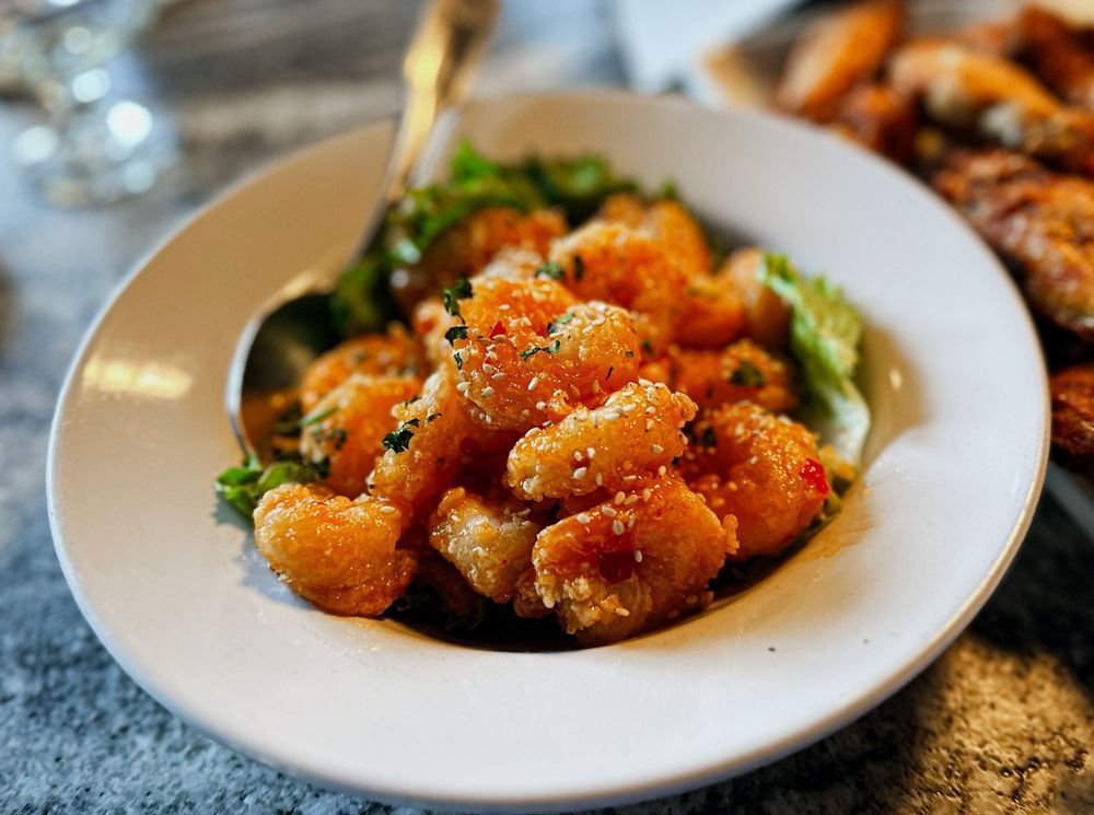 Plate of fried shrimp in a sauce, garnished with lettuce and sesame seeds, with a spoon.