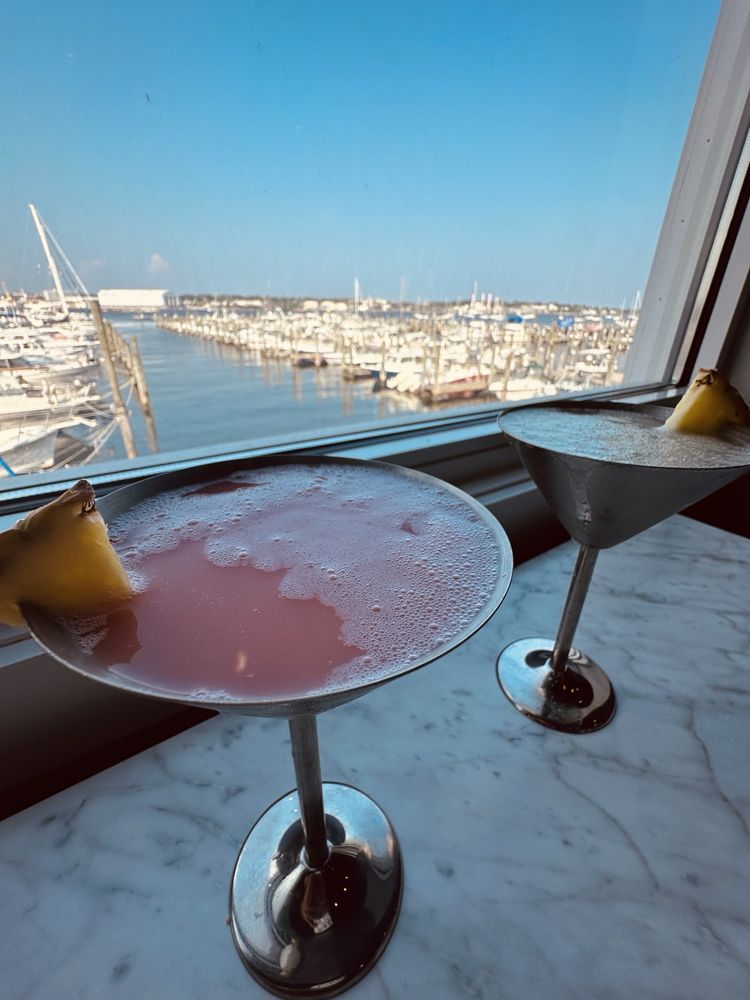 Two cocktails with pineapple garnish, overlooking a harbor with boats and a blue sky.